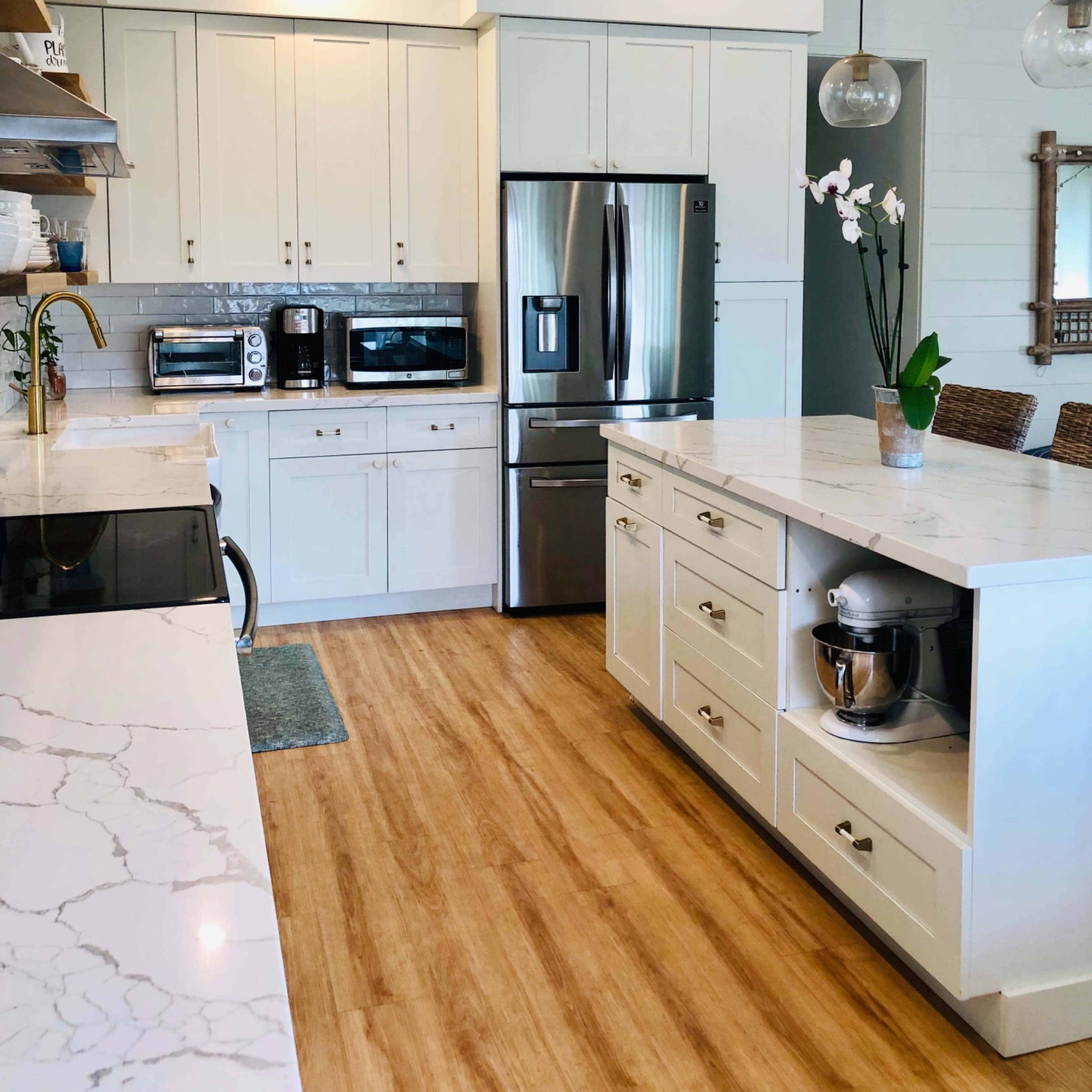A modern kitchen features white cabinetry, stainless steel appliances, and a large island with a marble countertop.