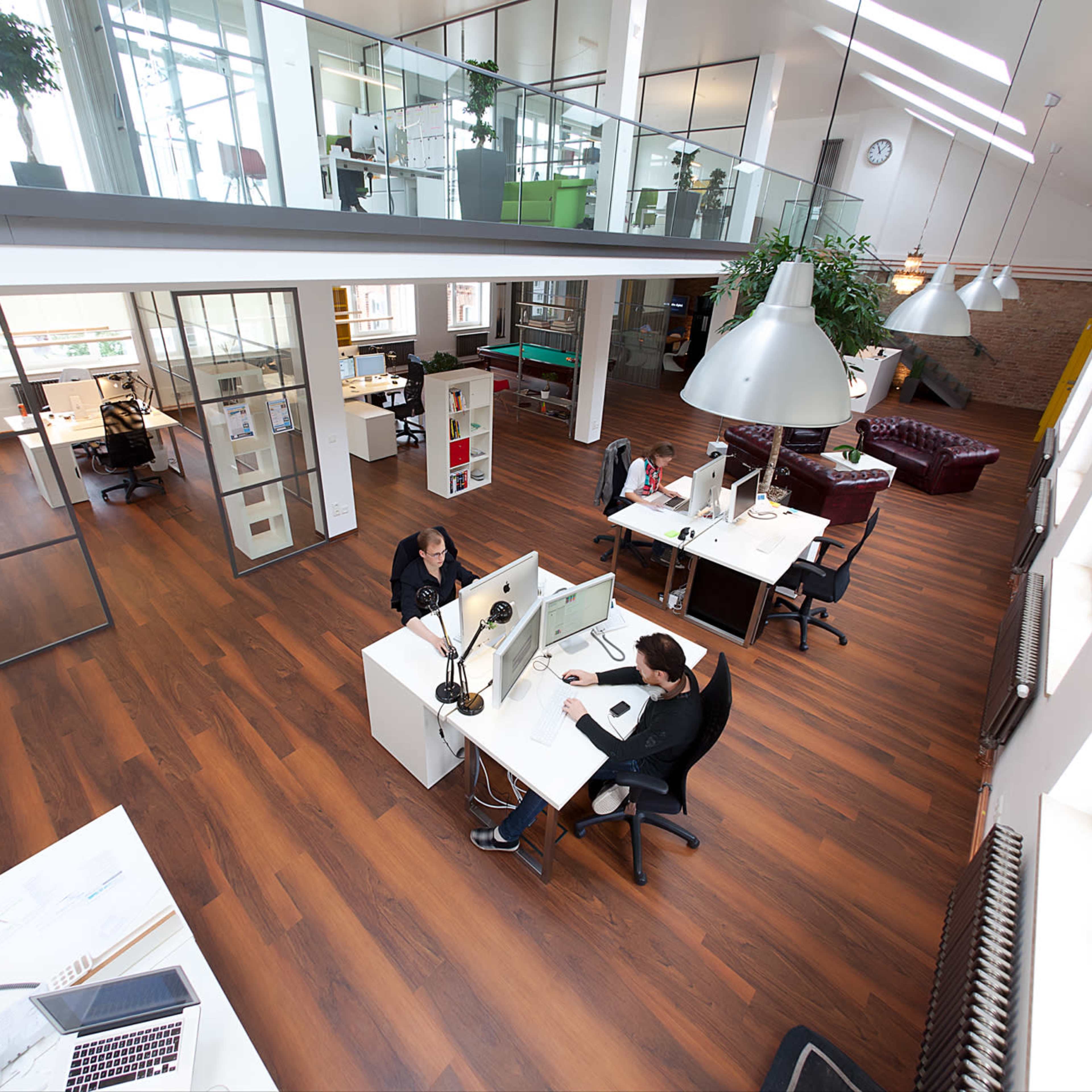 A modern office space with several workstations, large windows, and a mix of open and enclosed areas.