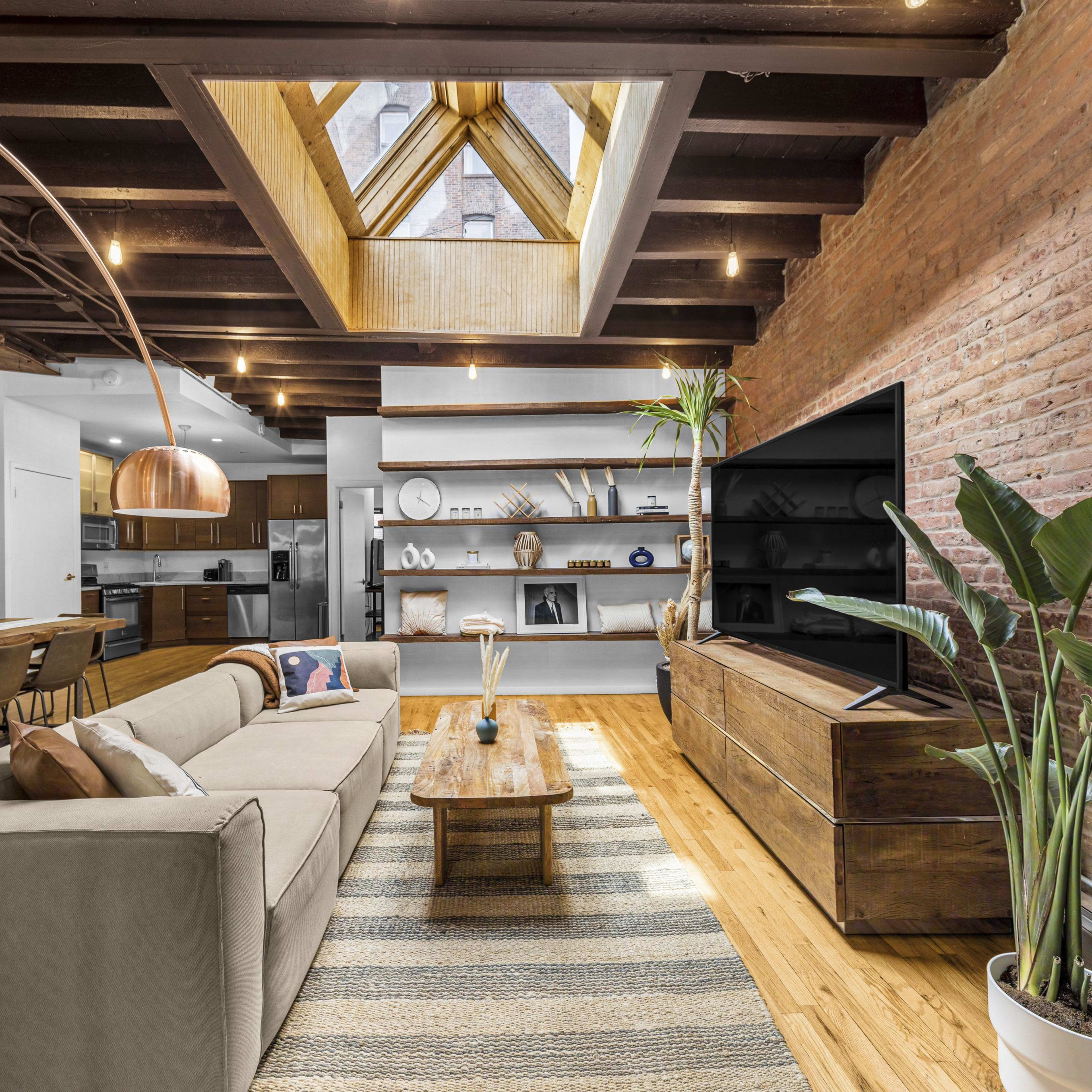 The living room features a cozy sectional sofa, a wooden coffee table, a large TV, and a skylight, with exposed beams and a mix of modern and rustic decor.