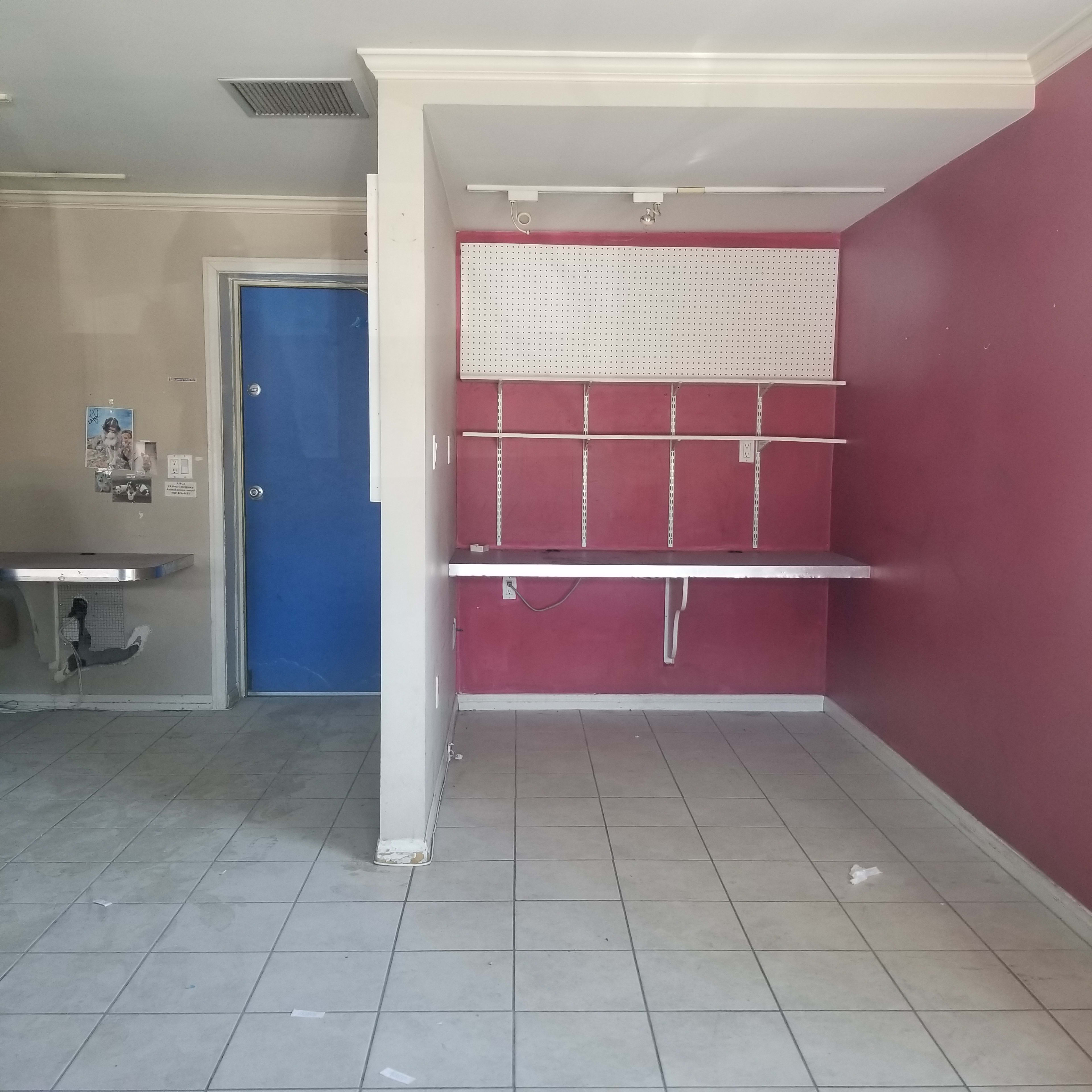 An empty room with pink walls, a blue door, and a metal table on the left.
