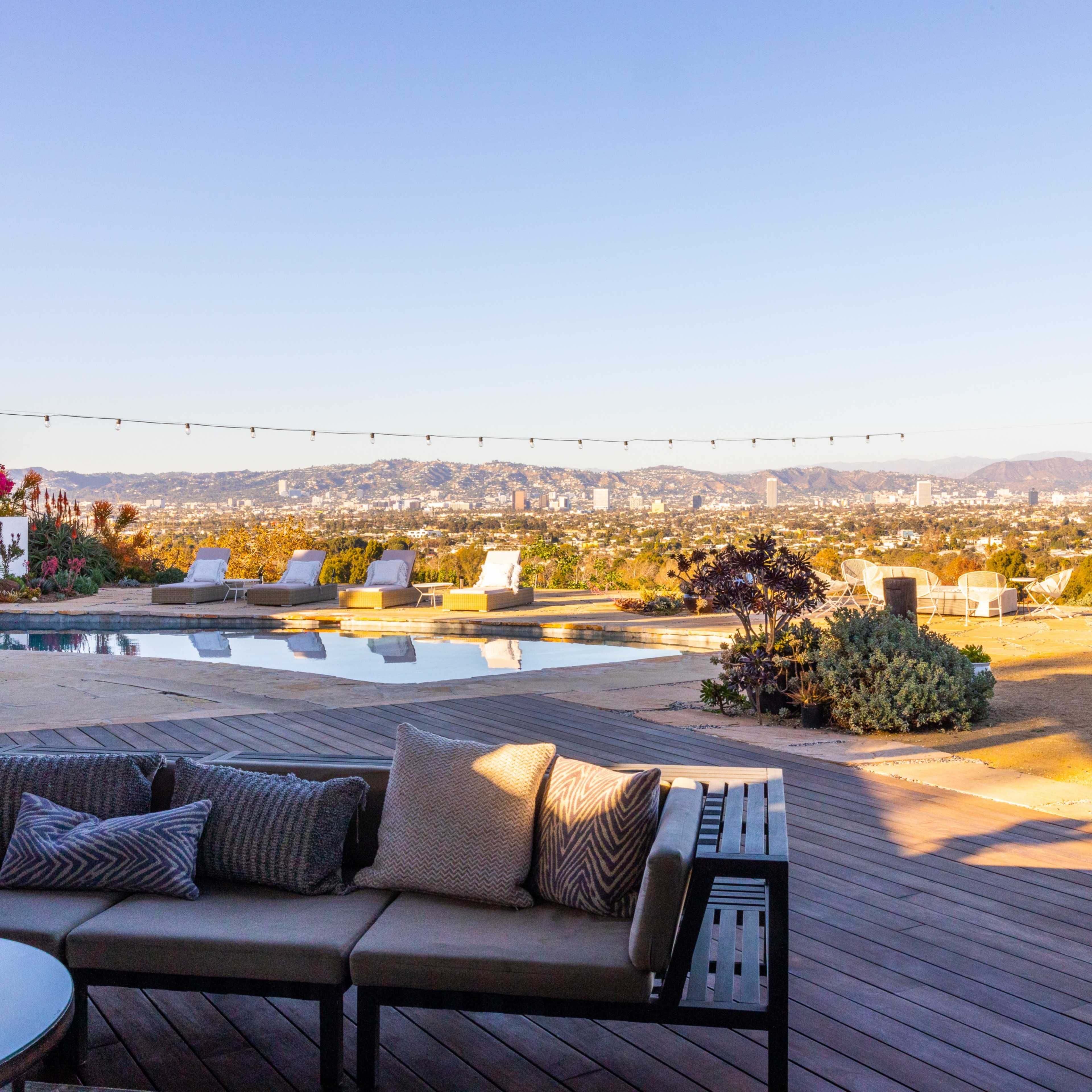 A patio with outdoor seating and a pool, overlooking a cityscape at sunset.
