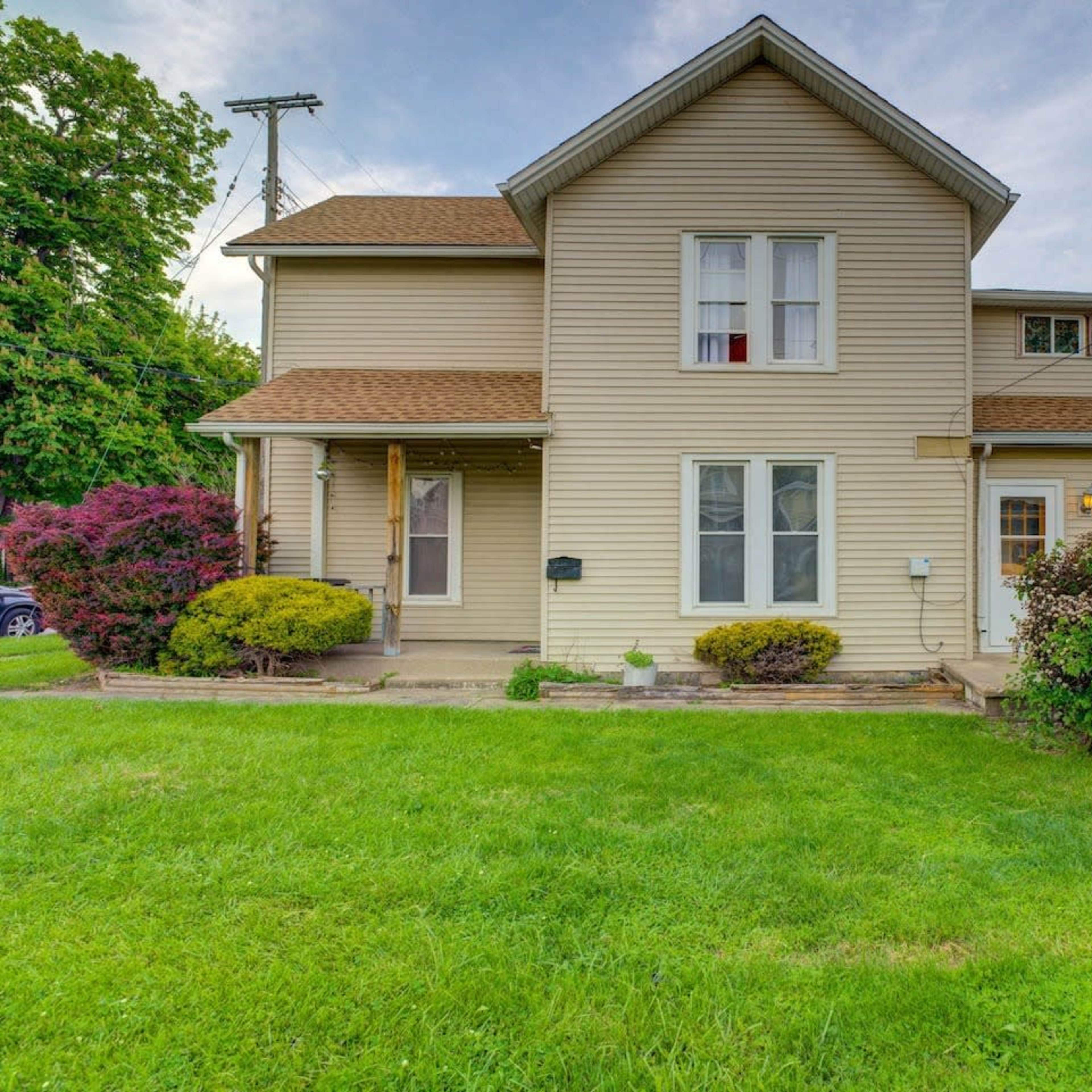 A two-story house with beige siding and a well-maintained front yard featuring bushes and grass.