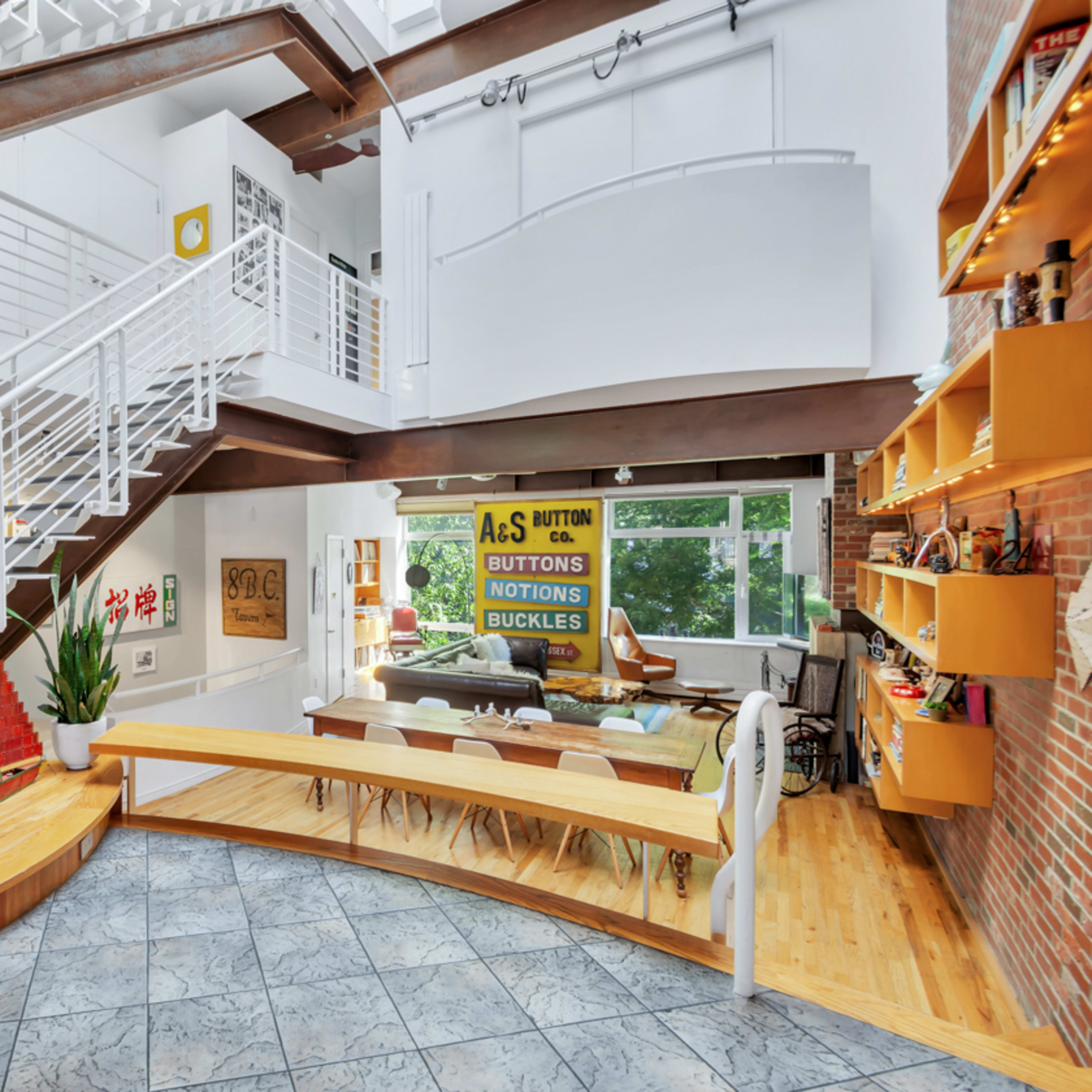A modern open-concept home features a wooden staircase, a large dining area, and a mix of greenery and decor elements.