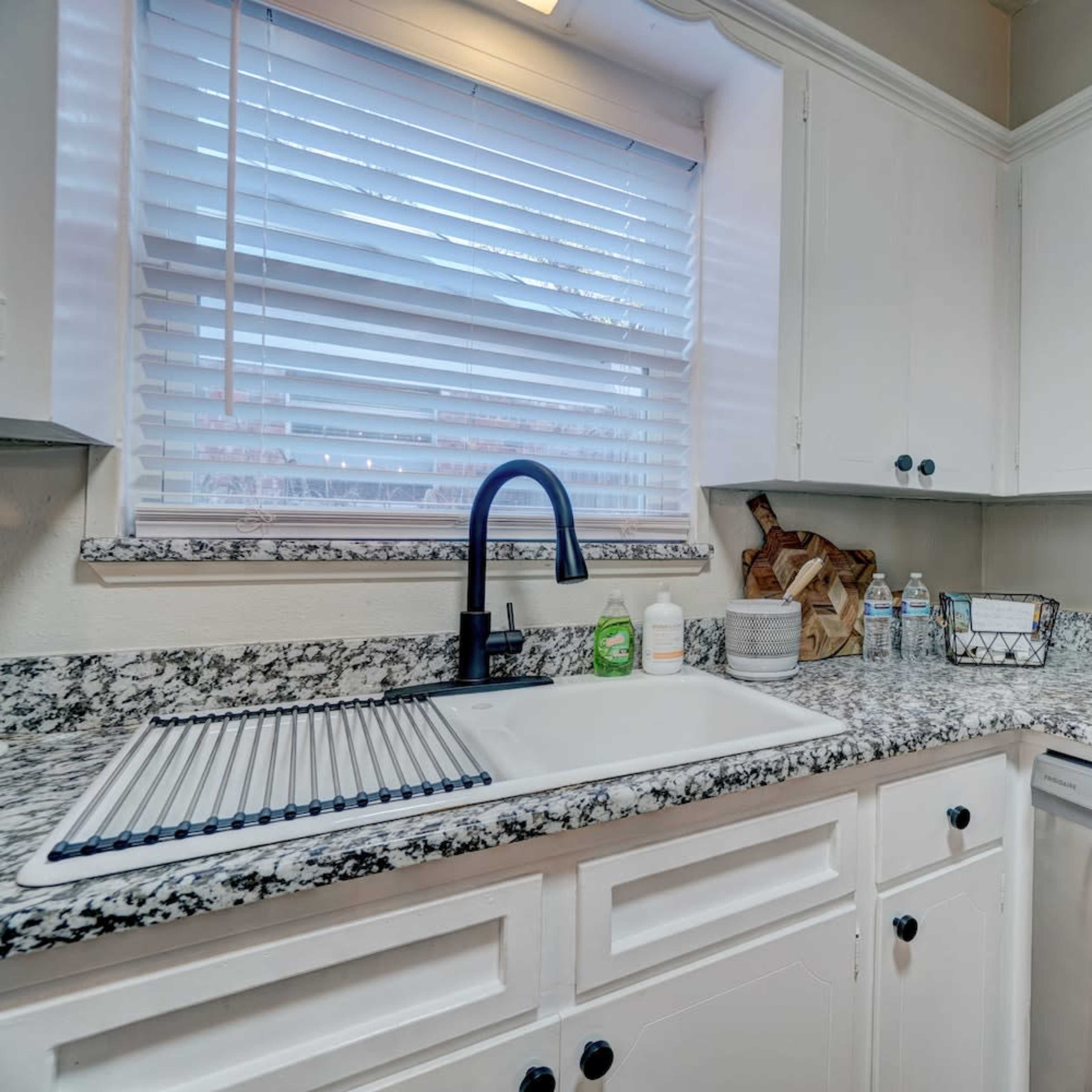 A kitchen featuring white cabinets, a granite countertop, a double sink, and various kitchen appliances including a coffee maker and a kettle.