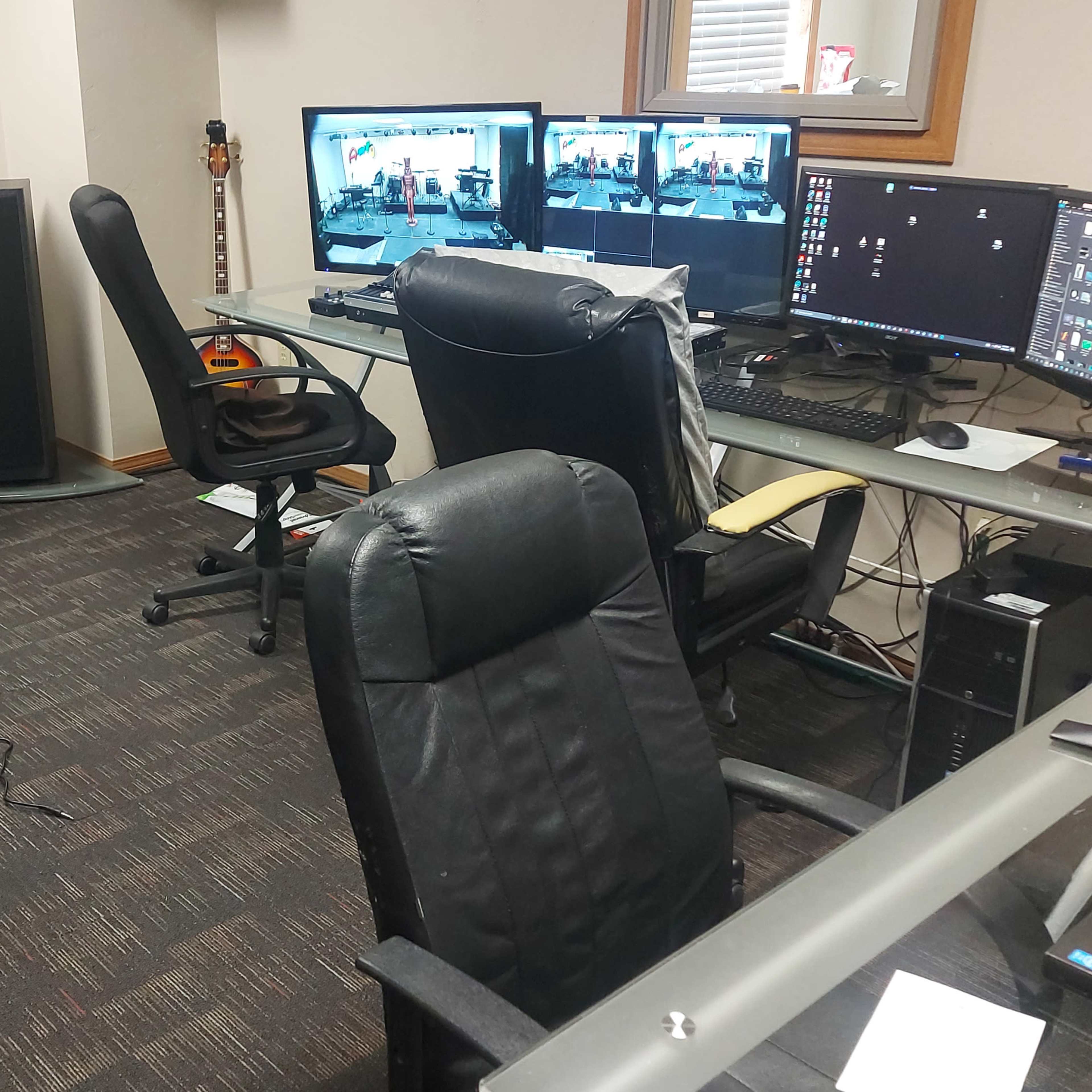A room equipped with multiple computer monitors, a sound mixer, and several office chairs.