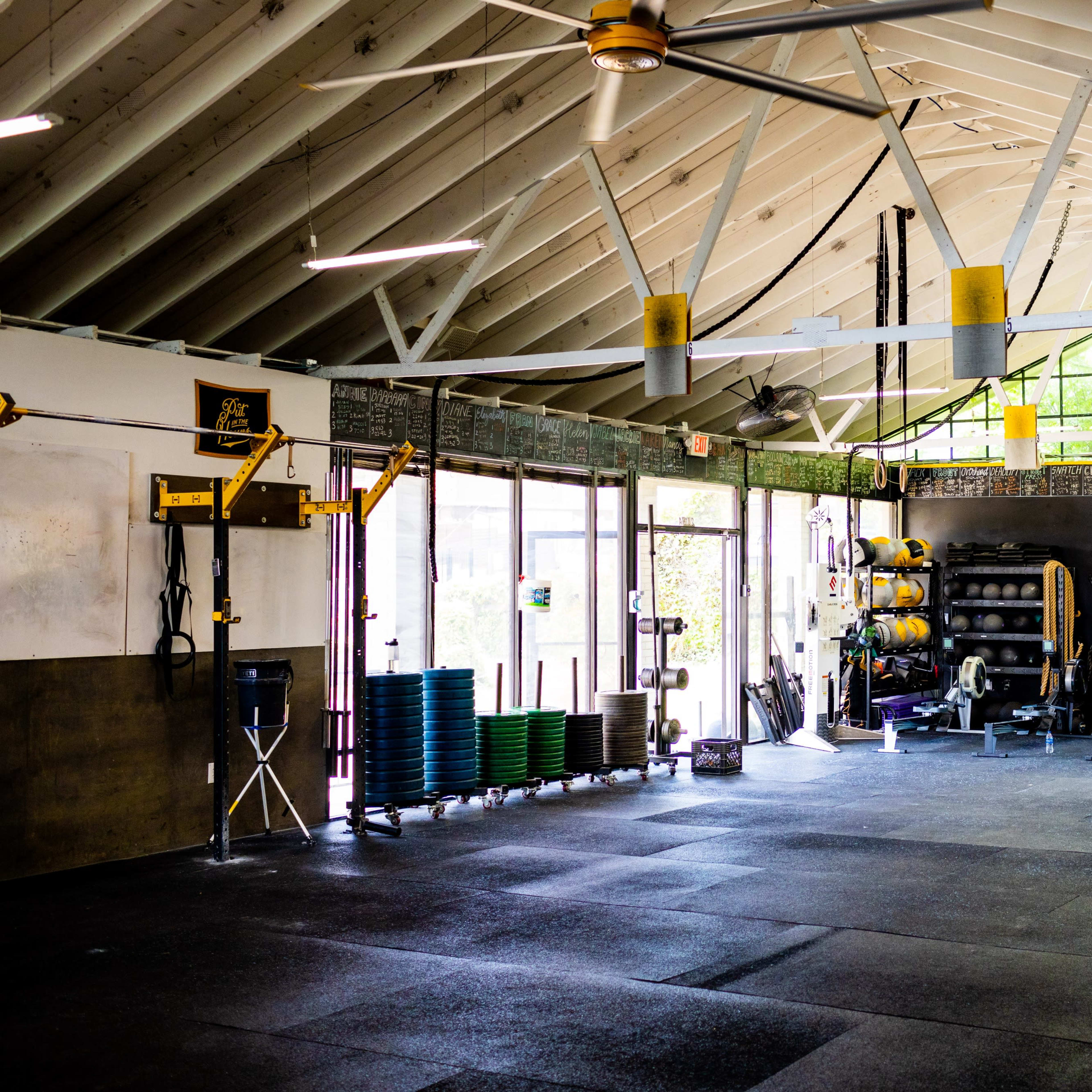 A spacious gym with various exercise equipment, large windows letting in natural light, and a rubber floor matting.