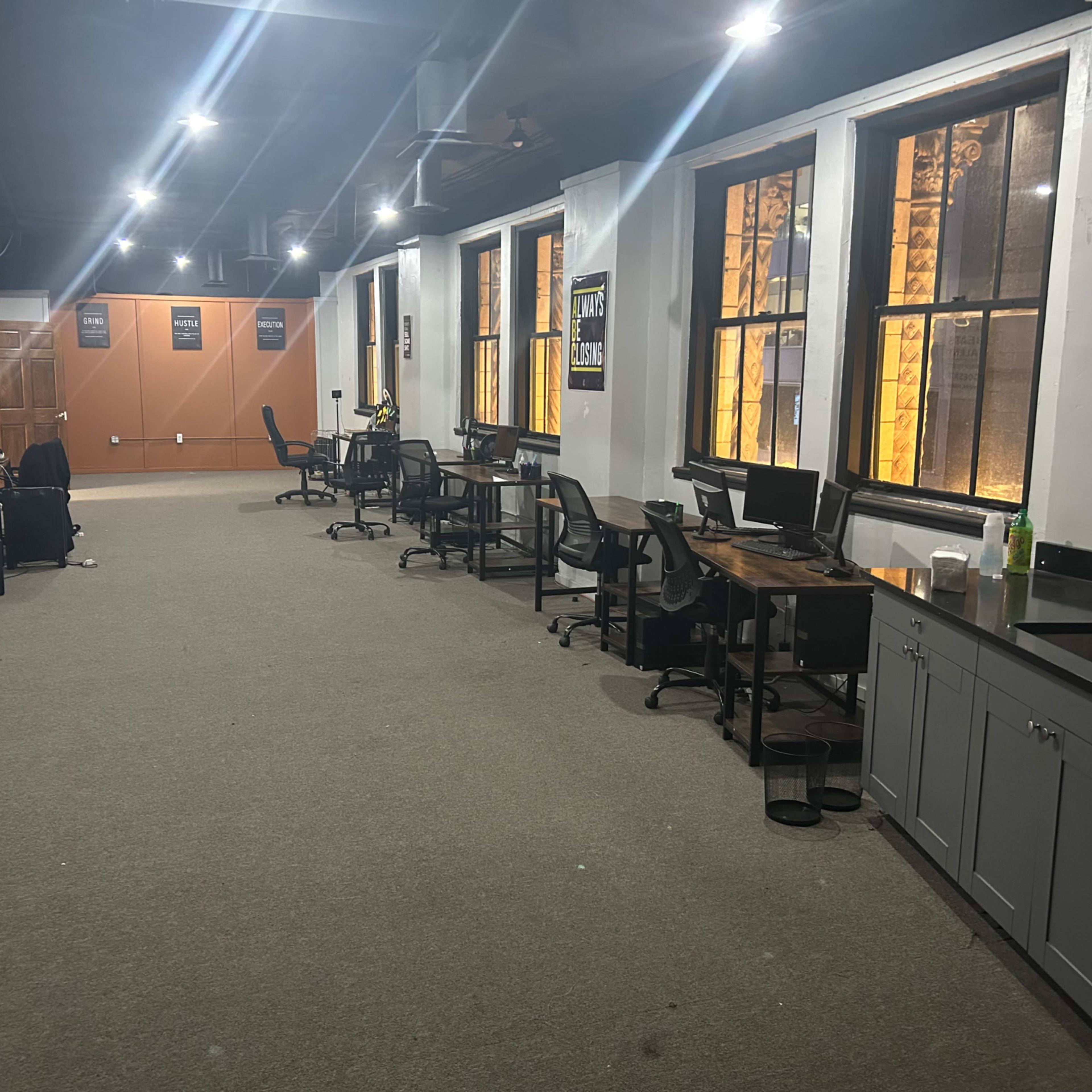 A large, empty office space with several desks, computers, and illuminated windows.