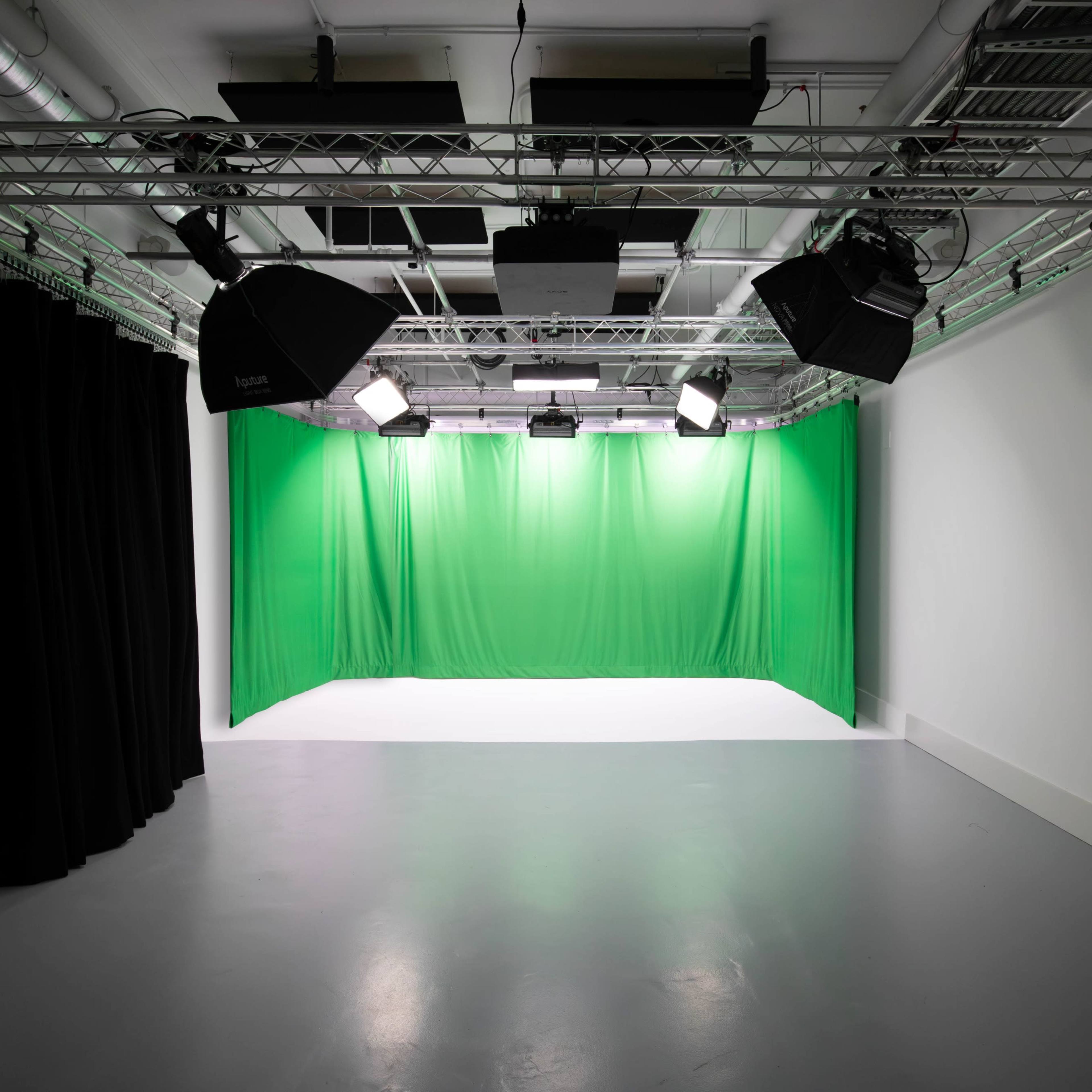 A photography studio with a white backdrop, multiple lighting fixtures, and green and black curtains.
