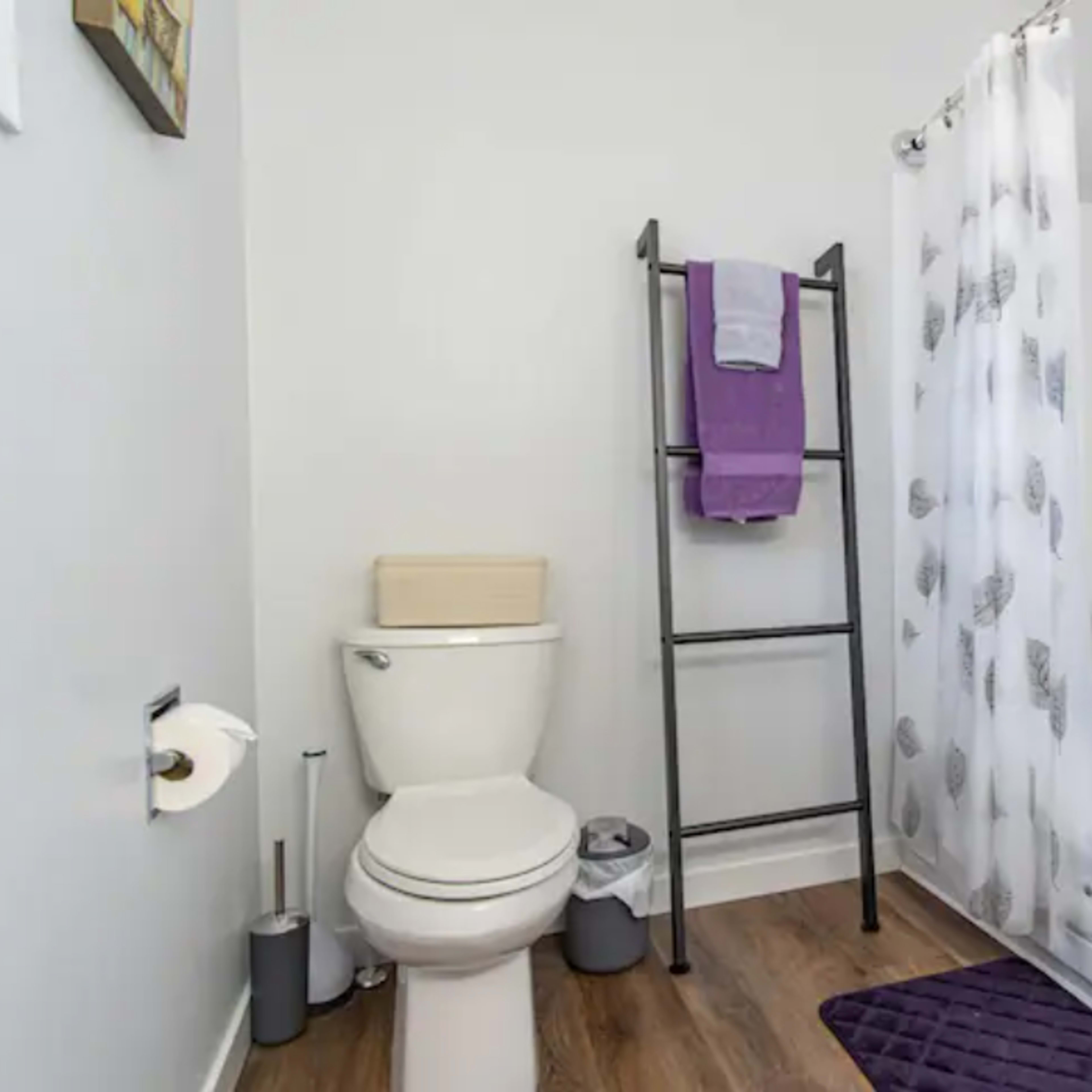 A bathroom featuring a toilet, a shower with a curtain, a towel rack with purple towels, and a bathtub.