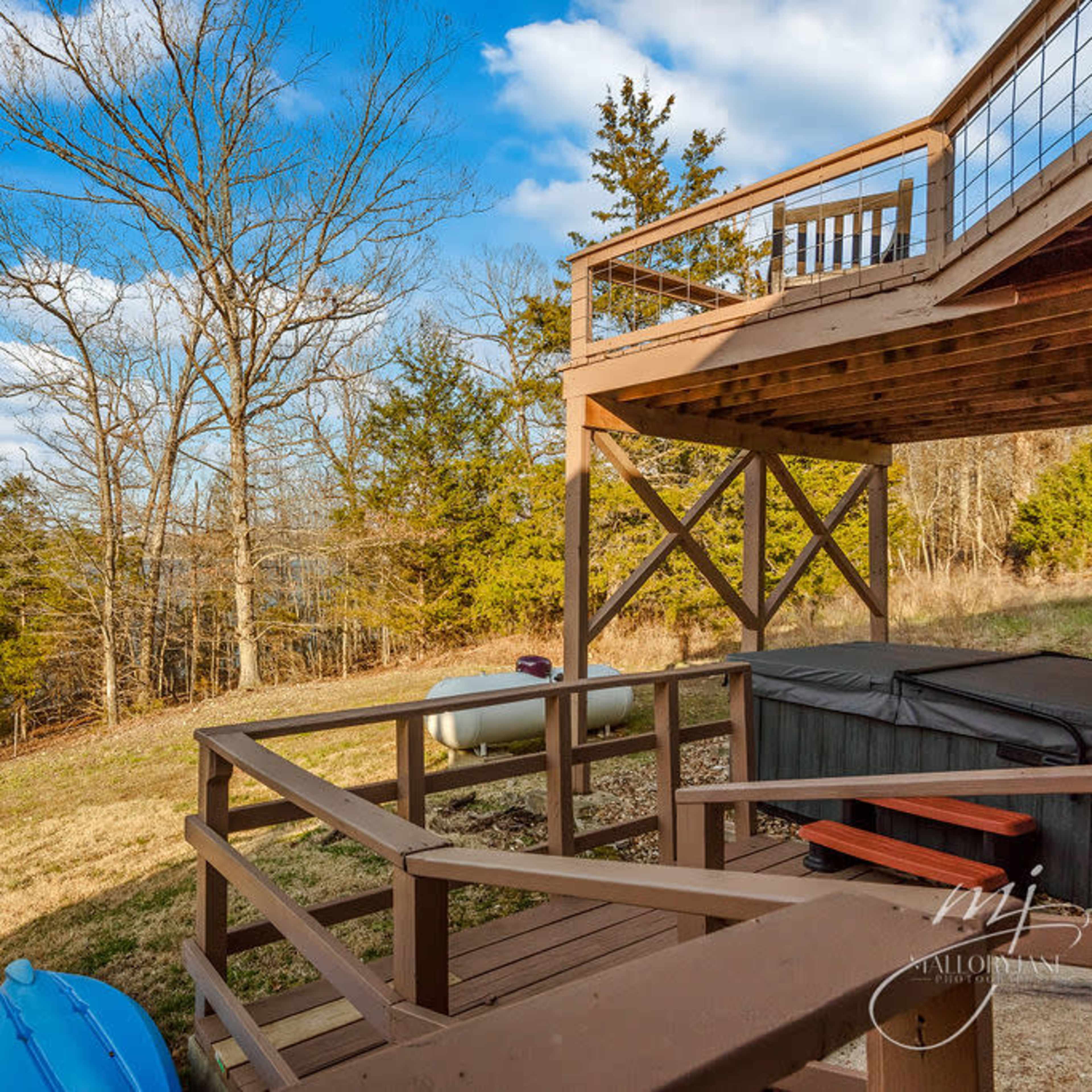 A wooden deck overlooking a lake, with two blue kayaks stored beside it and trees lining the shore.