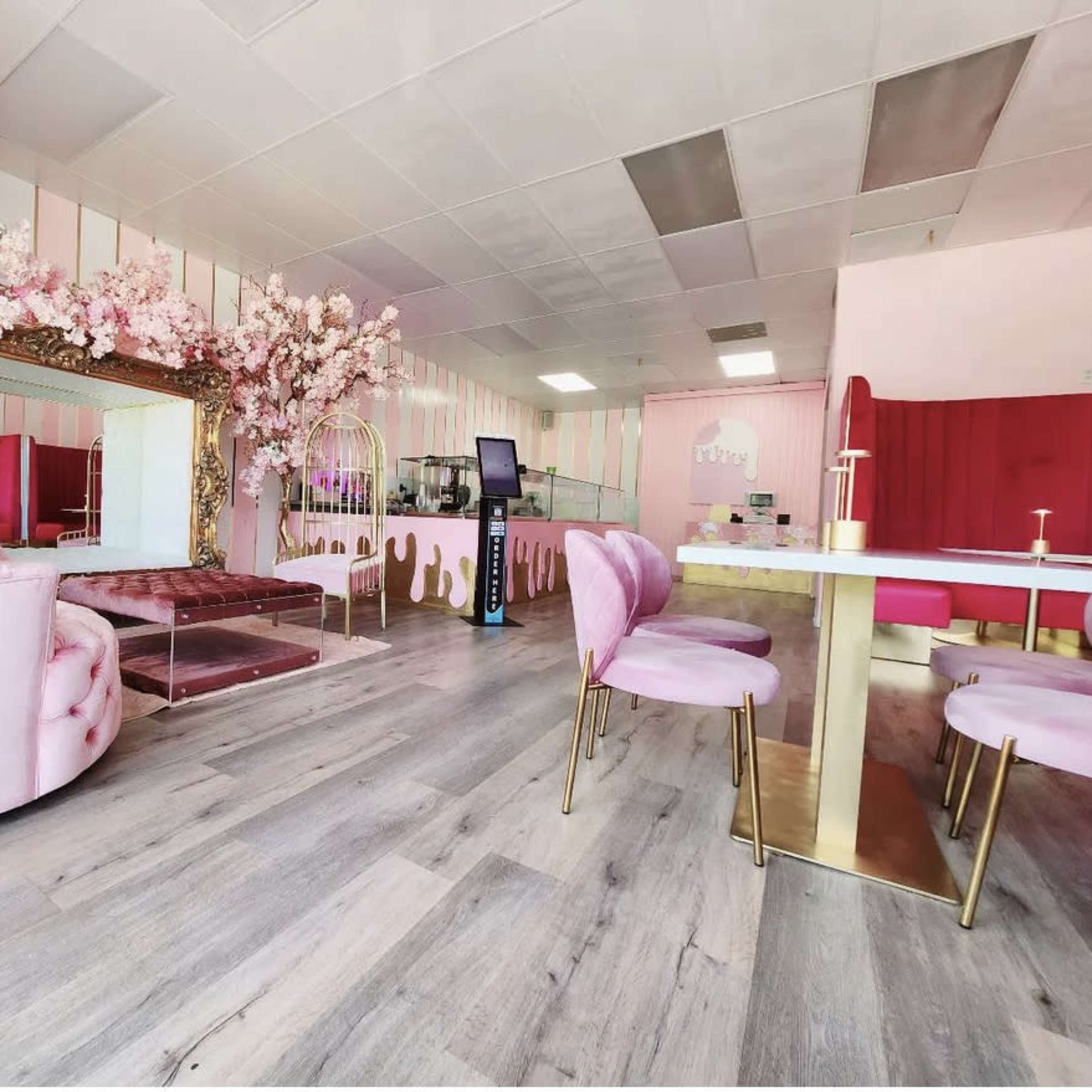 A pastel pink-themed cafe interior featuring plush seating, a large decorative mirror, and floral accents.