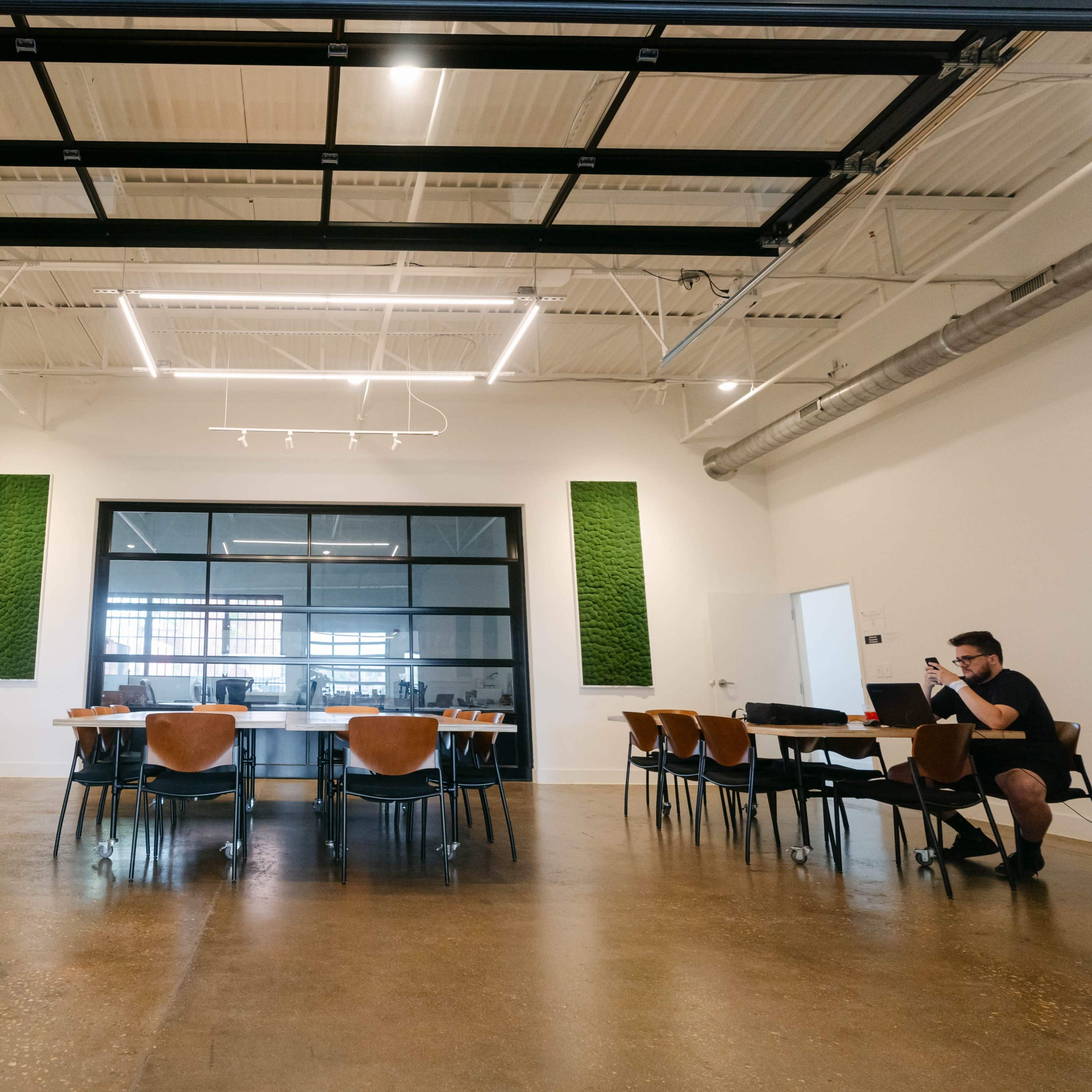 A spacious meeting room features a long table surrounded by chairs, with large windows and green wall accents.