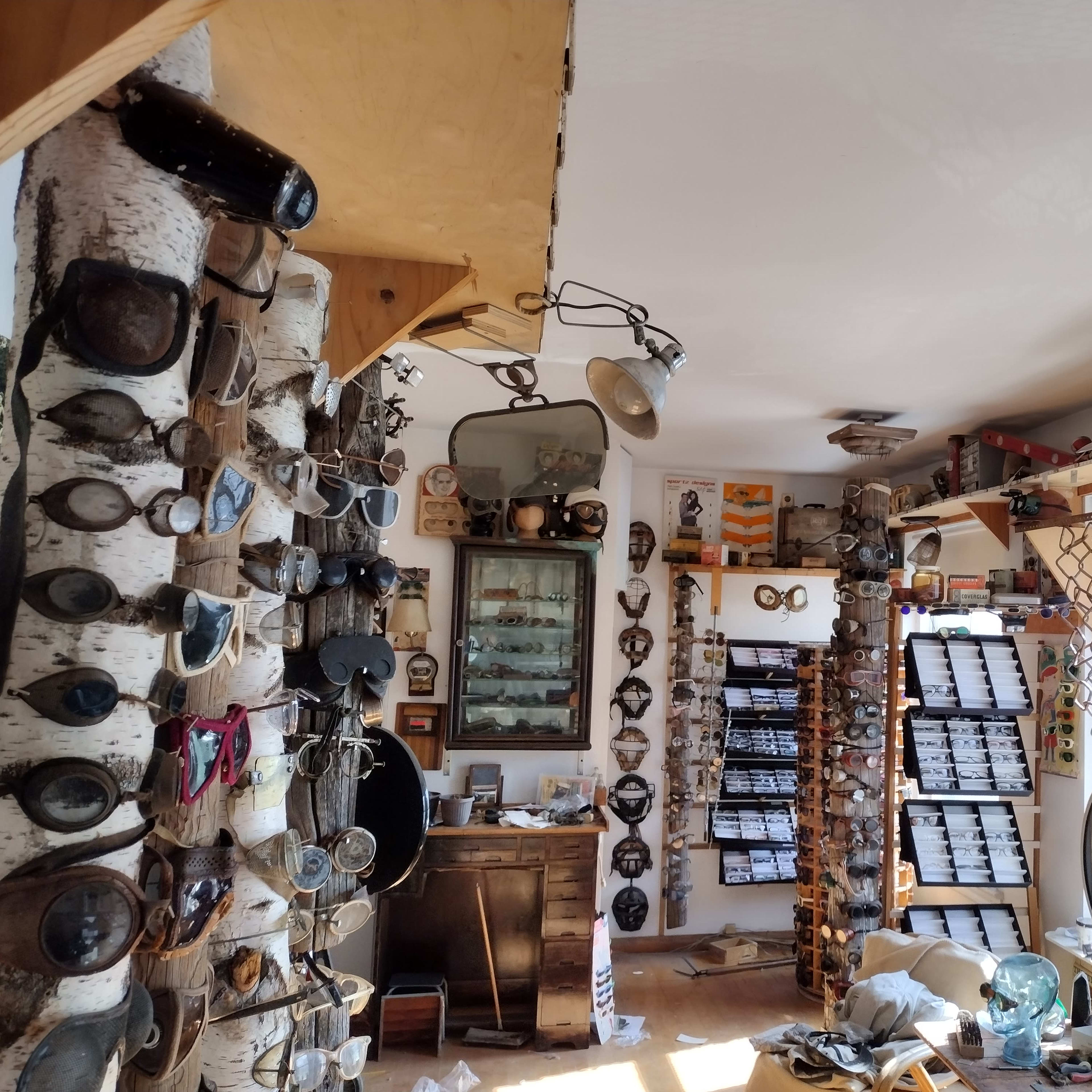 The room features wooden pillars adorned with various goggles and a wall lined with boxes, creating a cluttered yet organized workshop atmosphere.
