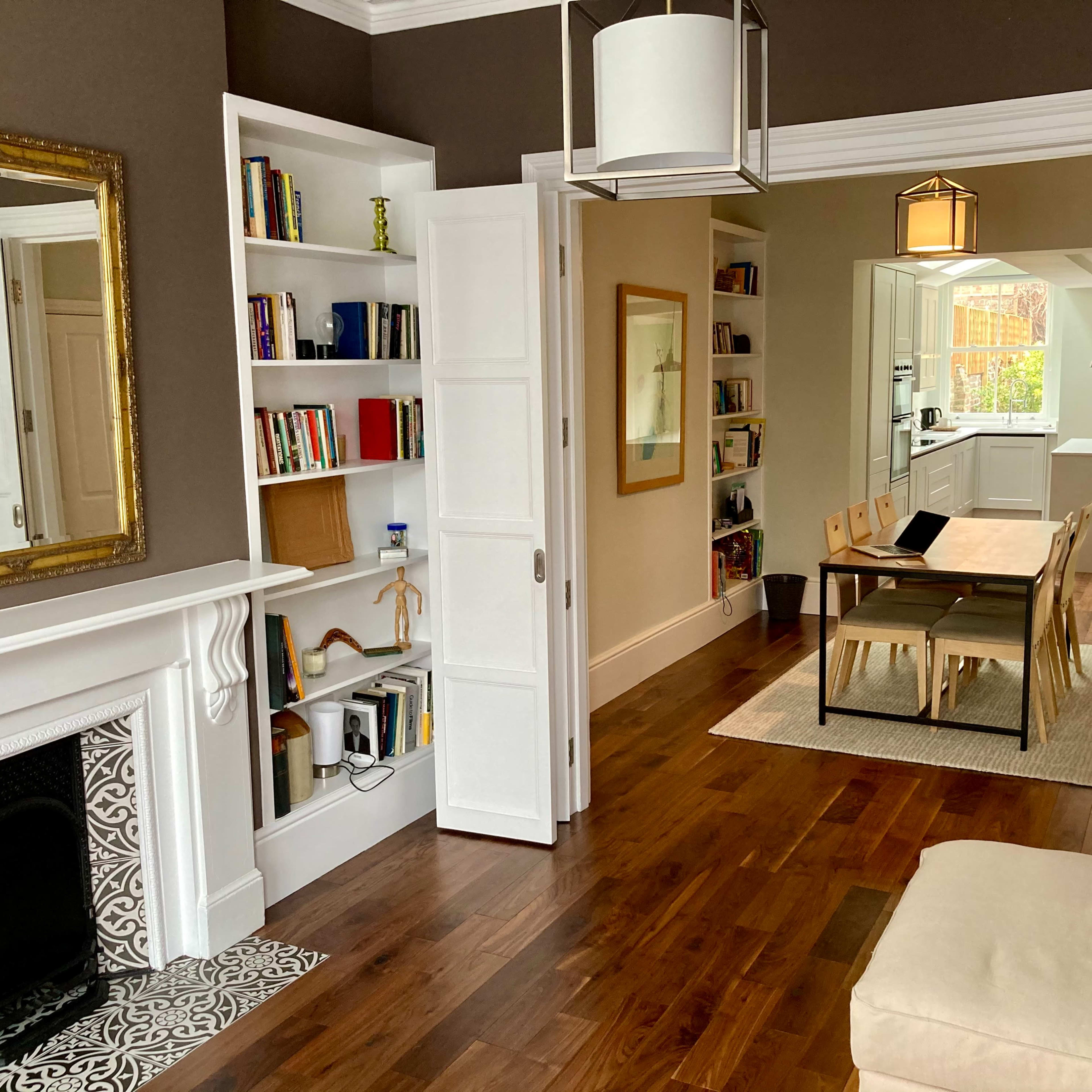 A cozy interior with a living room featuring a fireplace and bookshelves, leading to a dining area with a long table and open kitchen.
