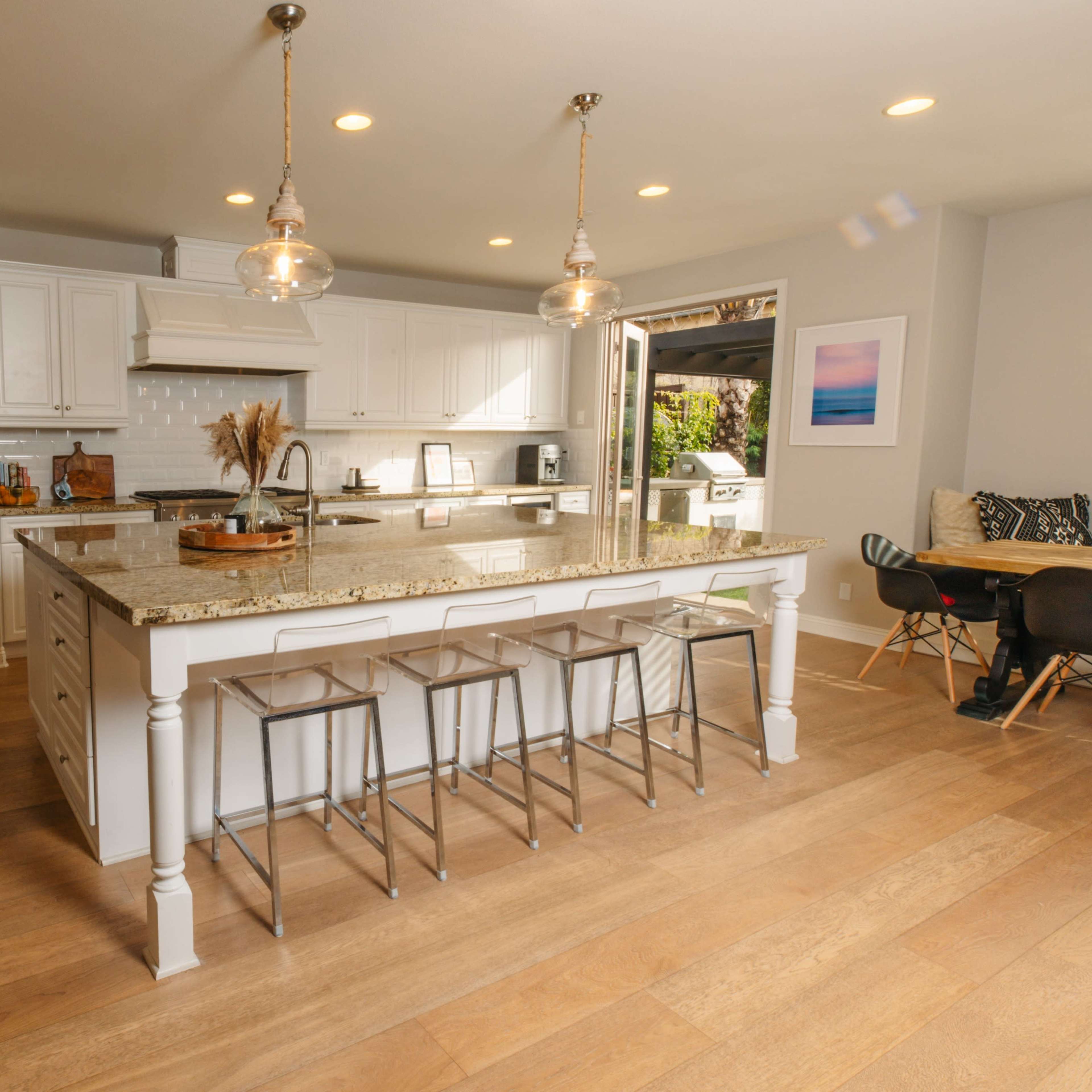 A modern kitchen features white cabinetry, a large island with seating, and an open layout leading to an outdoor area.