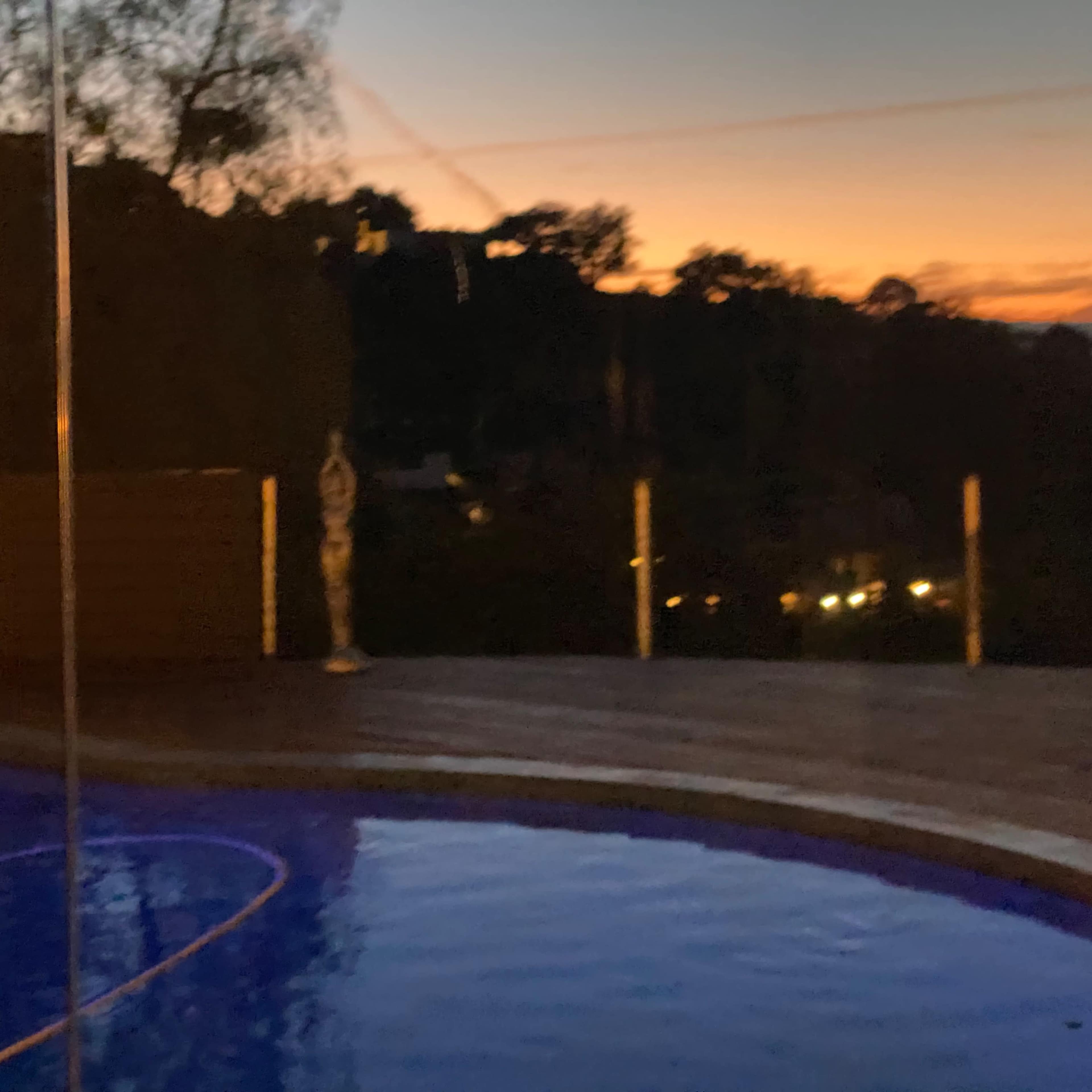 A swimming pool with blue water beneath a sunset sky, surrounded by glass fencing.