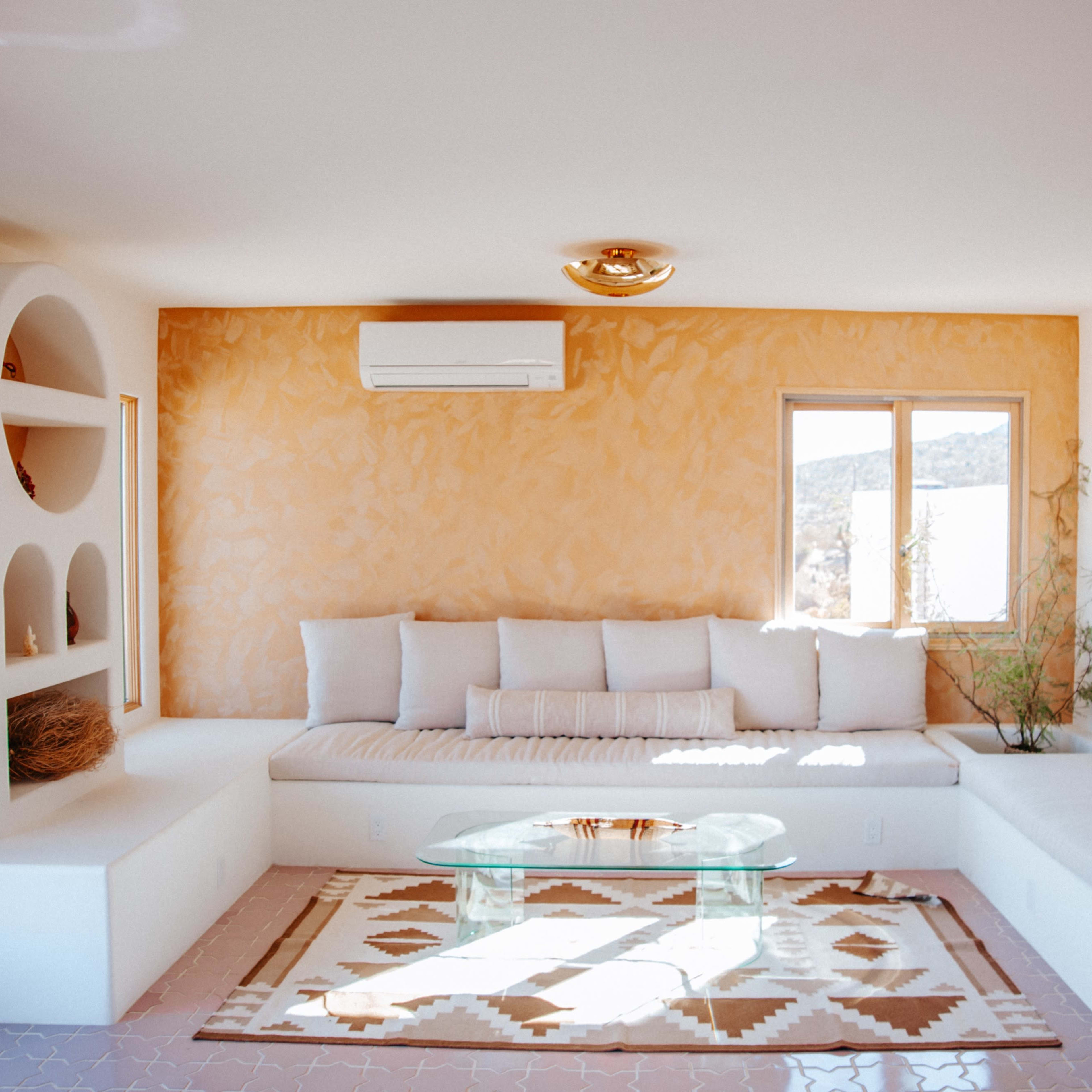 A modern living room with a beige sectional sofa, a glass coffee table, and decorative wall shelves against a light orange wall.