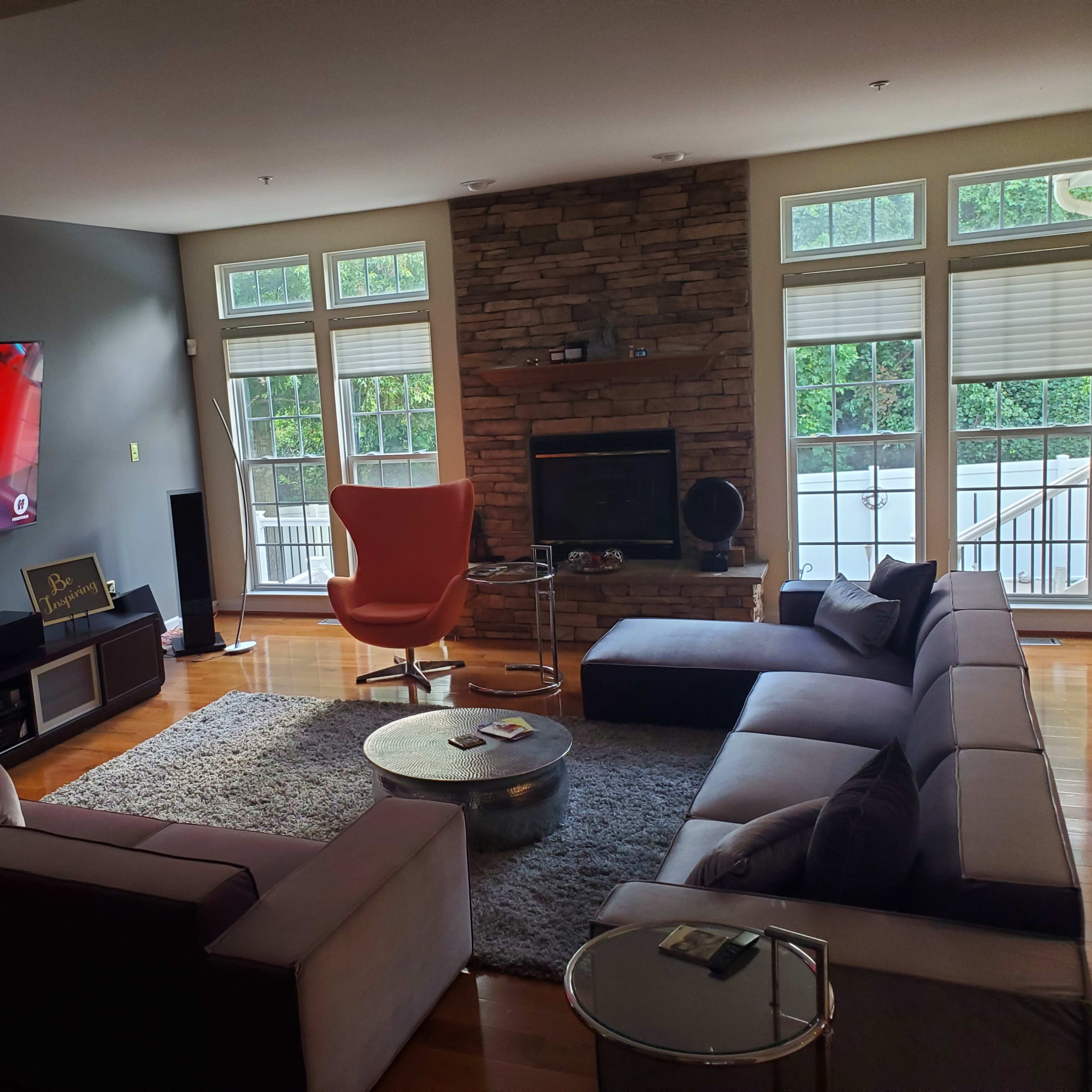 A modern living room with a large television mounted on the wall, a stone fireplace, a sectional sofa, and a distinctive orange armchair.