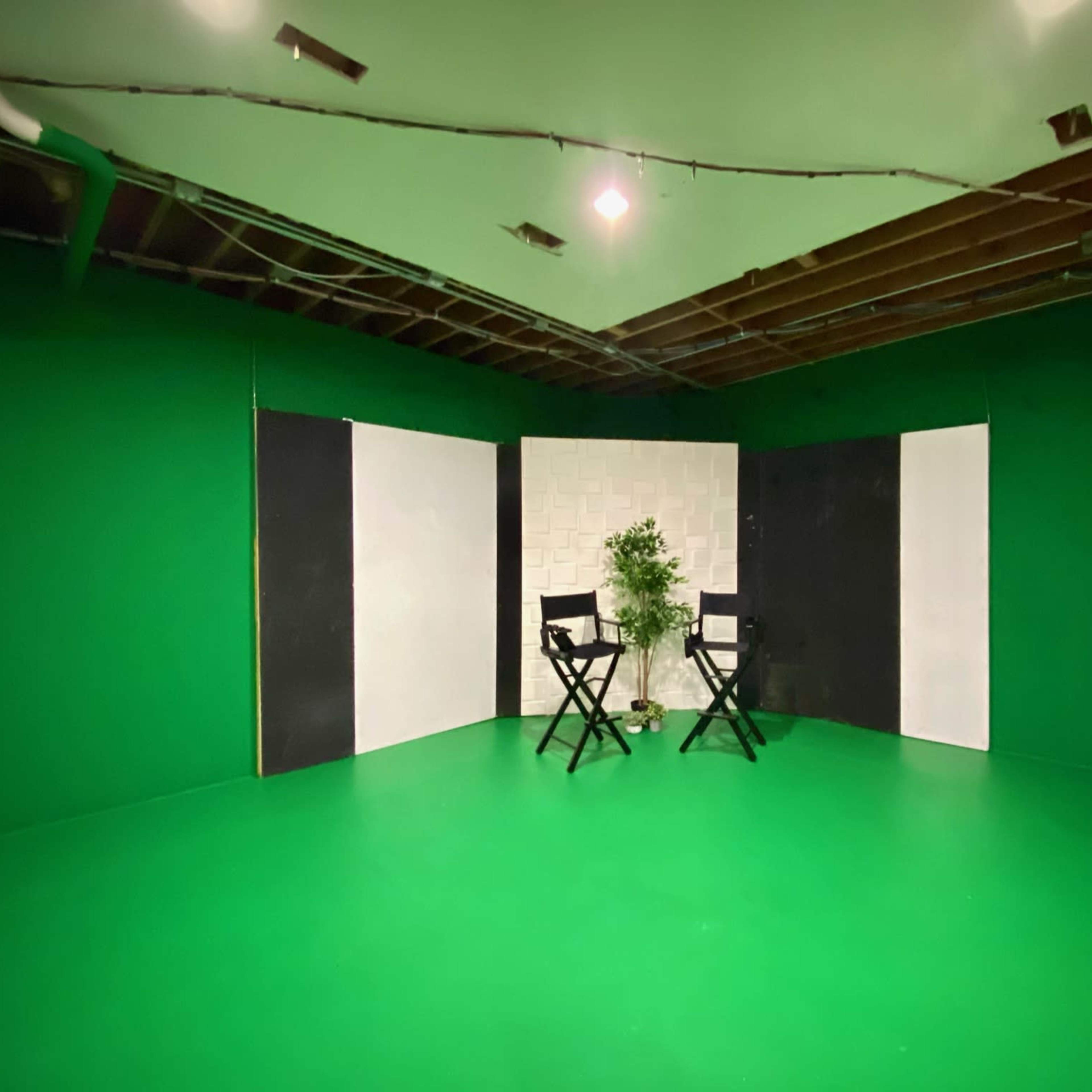 A minimalistic studio setup with two black director's chairs placed on a green floor, surrounded by green walls and a white textured backdrop.