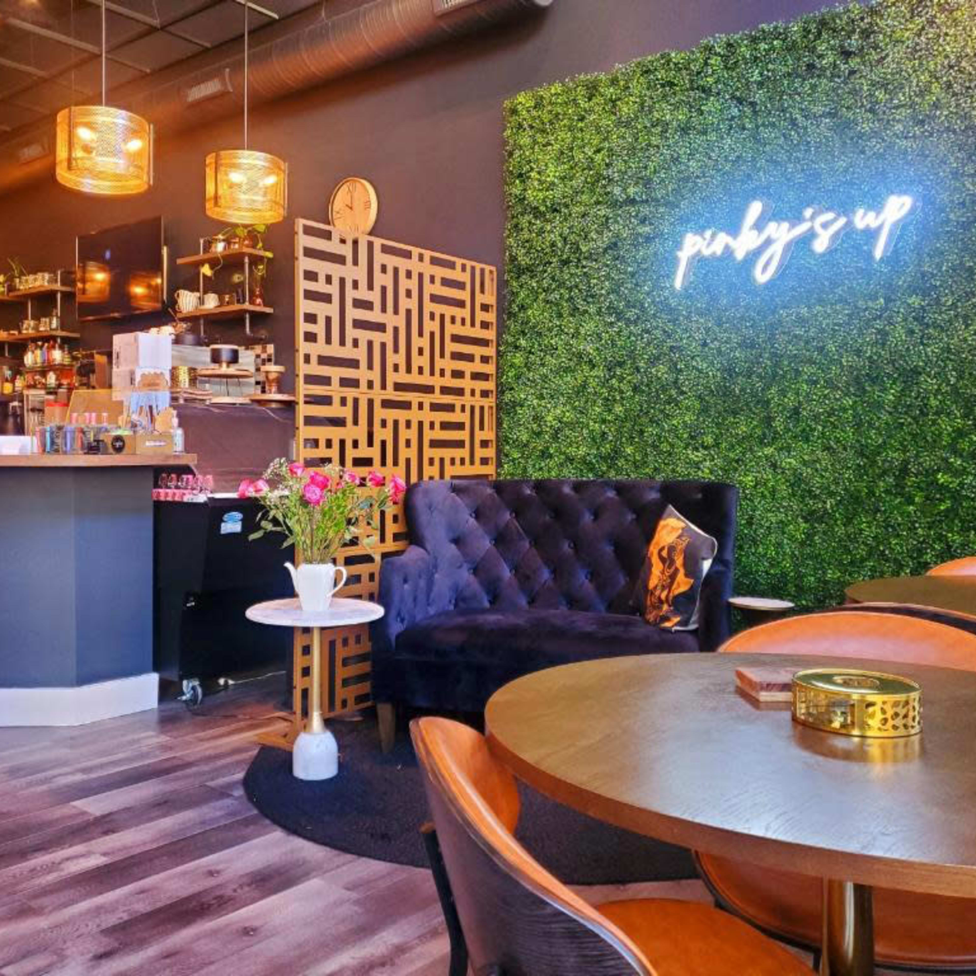 A modern café interior featuring a dark bar area, stylish seating, and a green wall with decorative lighting.