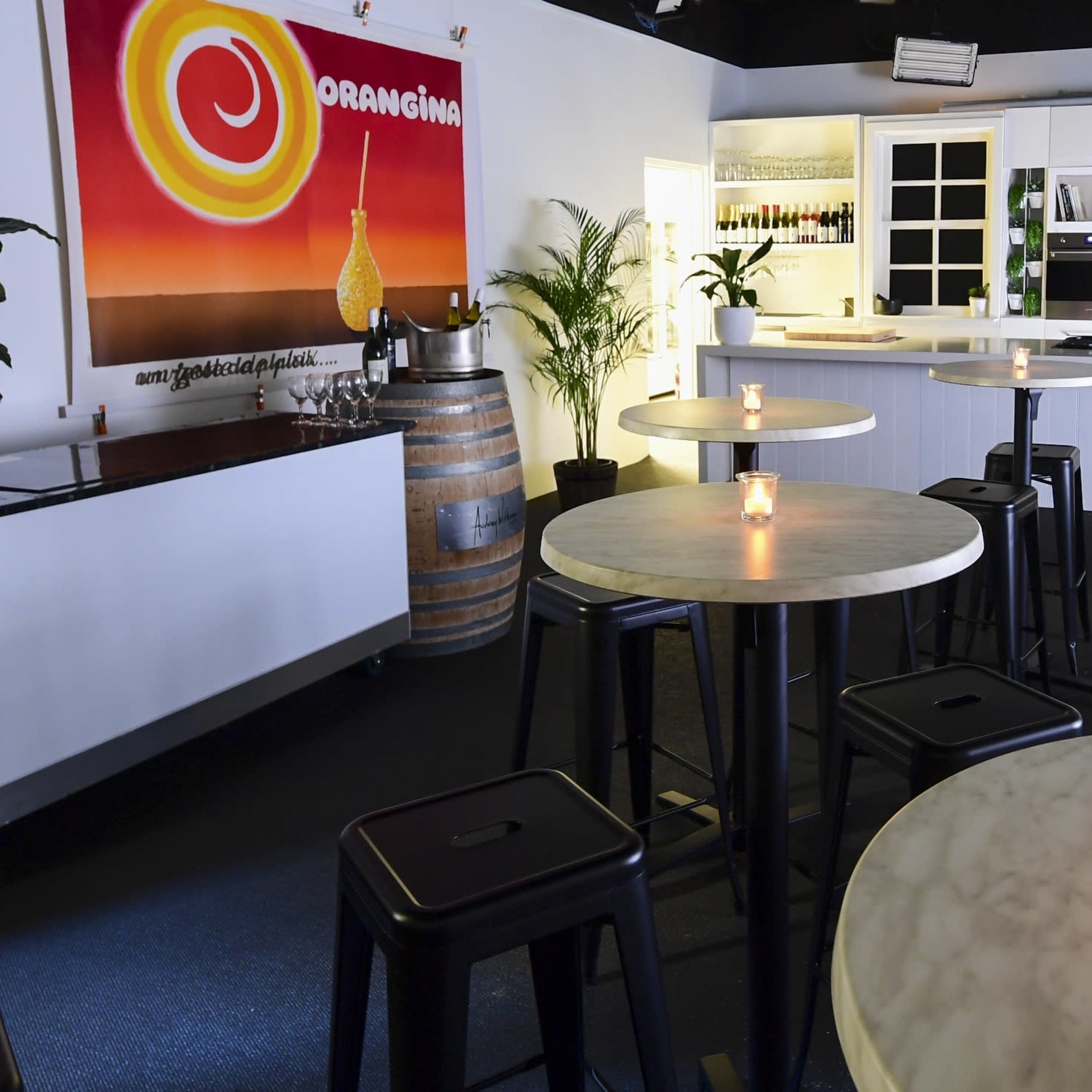 A modern bar area with round marble-top tables, black stools, and a brightly colored mural on the wall, illuminated by candles on the tables.