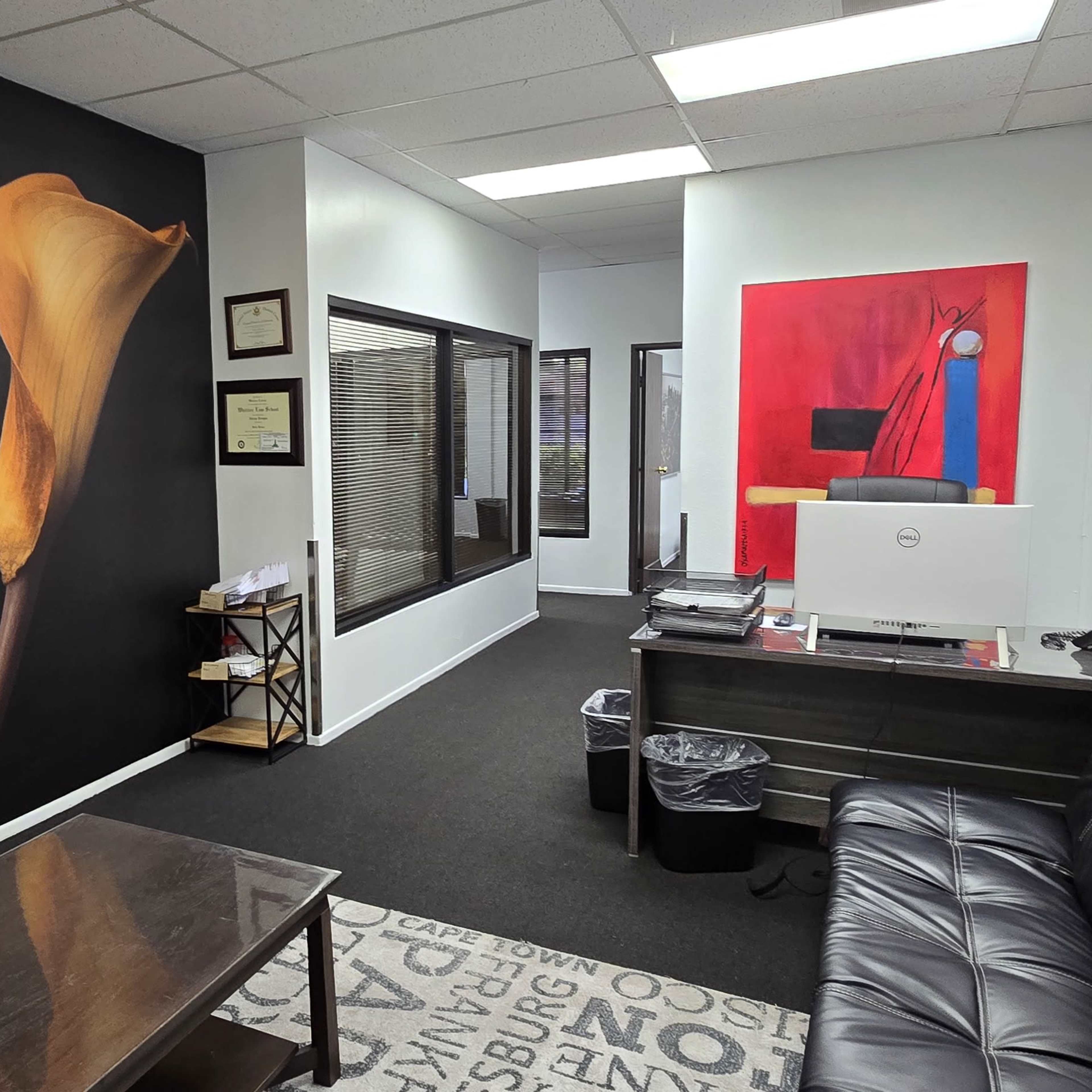 A modern office interior with a black wall featuring floral artwork, a reception area with a desk, and a seating area.