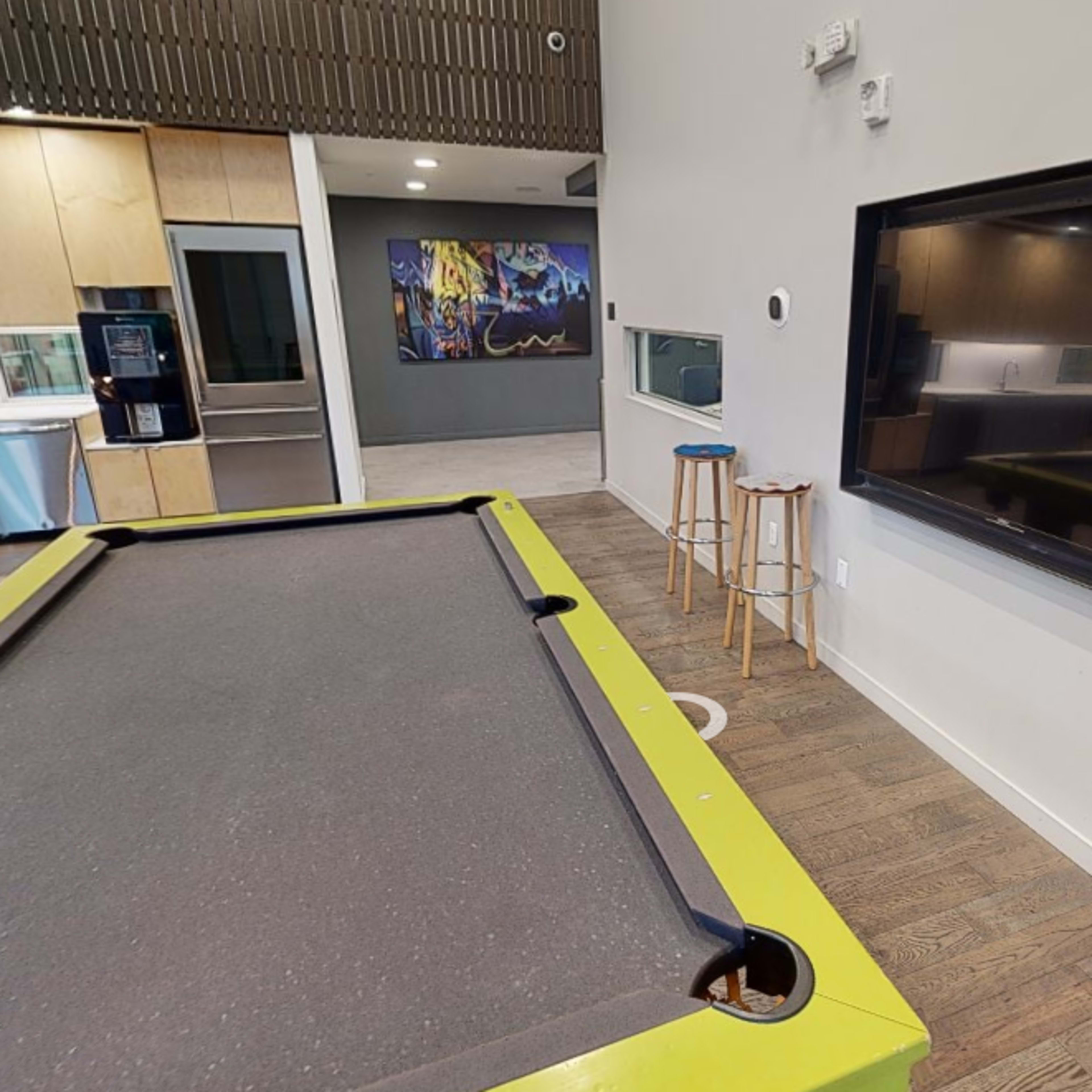 A modern game room featuring a green-edged pool table next to a large flat-screen TV mounted on the wall.