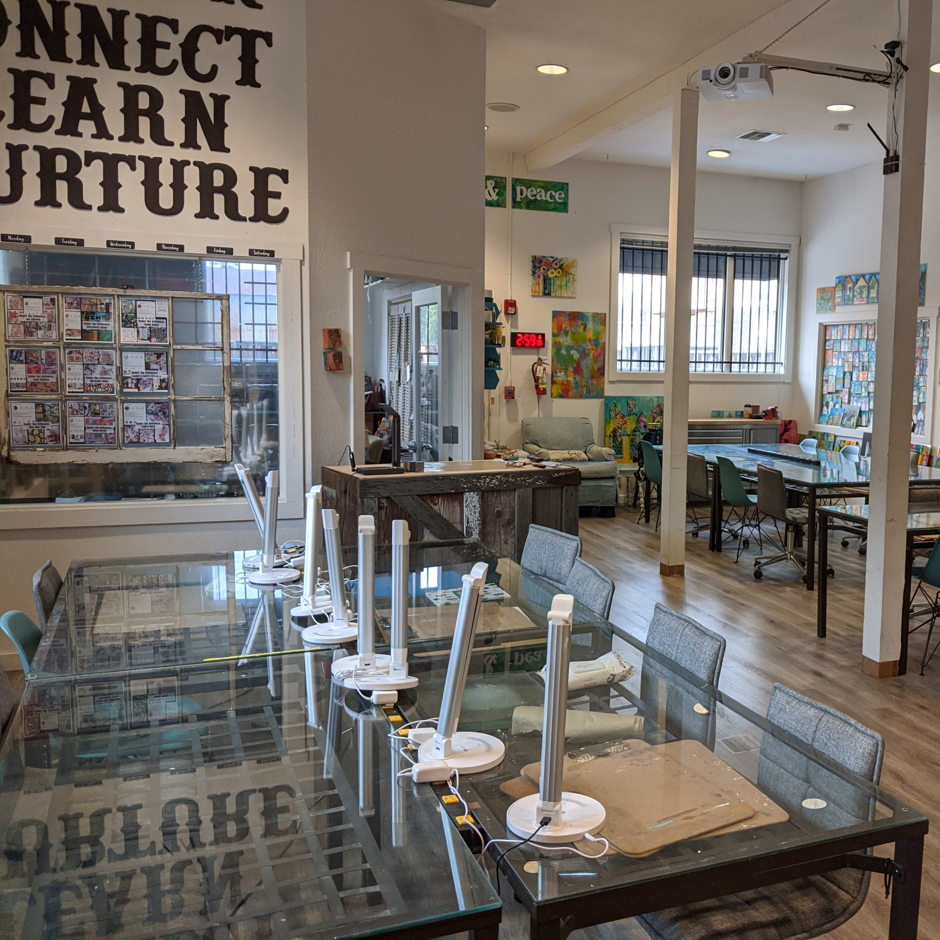 A spacious art classroom with several tables and chairs, displaying colorful artwork on the walls.