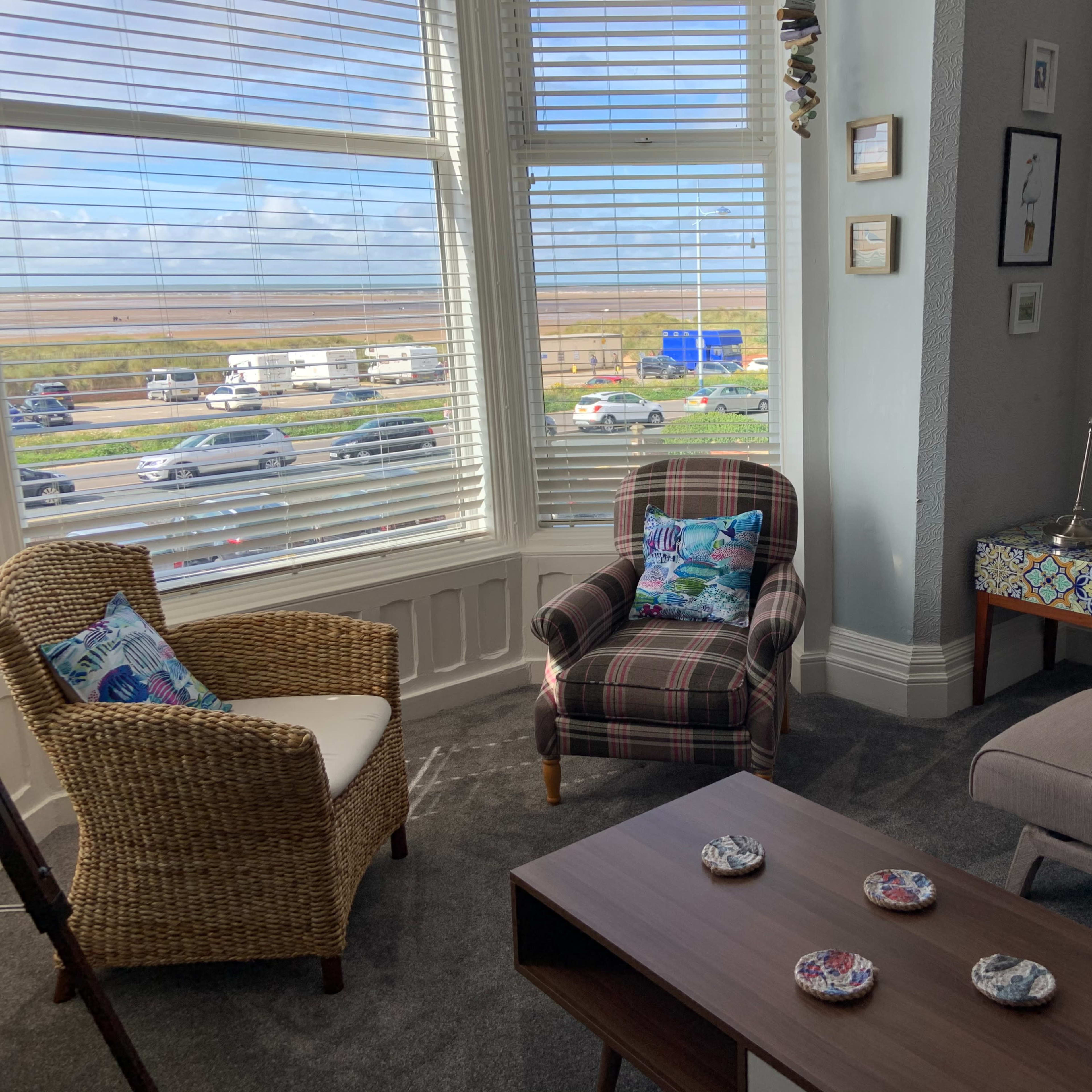 A cozy sitting area features two chairs, a coffee table, and a large window overlooking a busy road and scenic landscape.