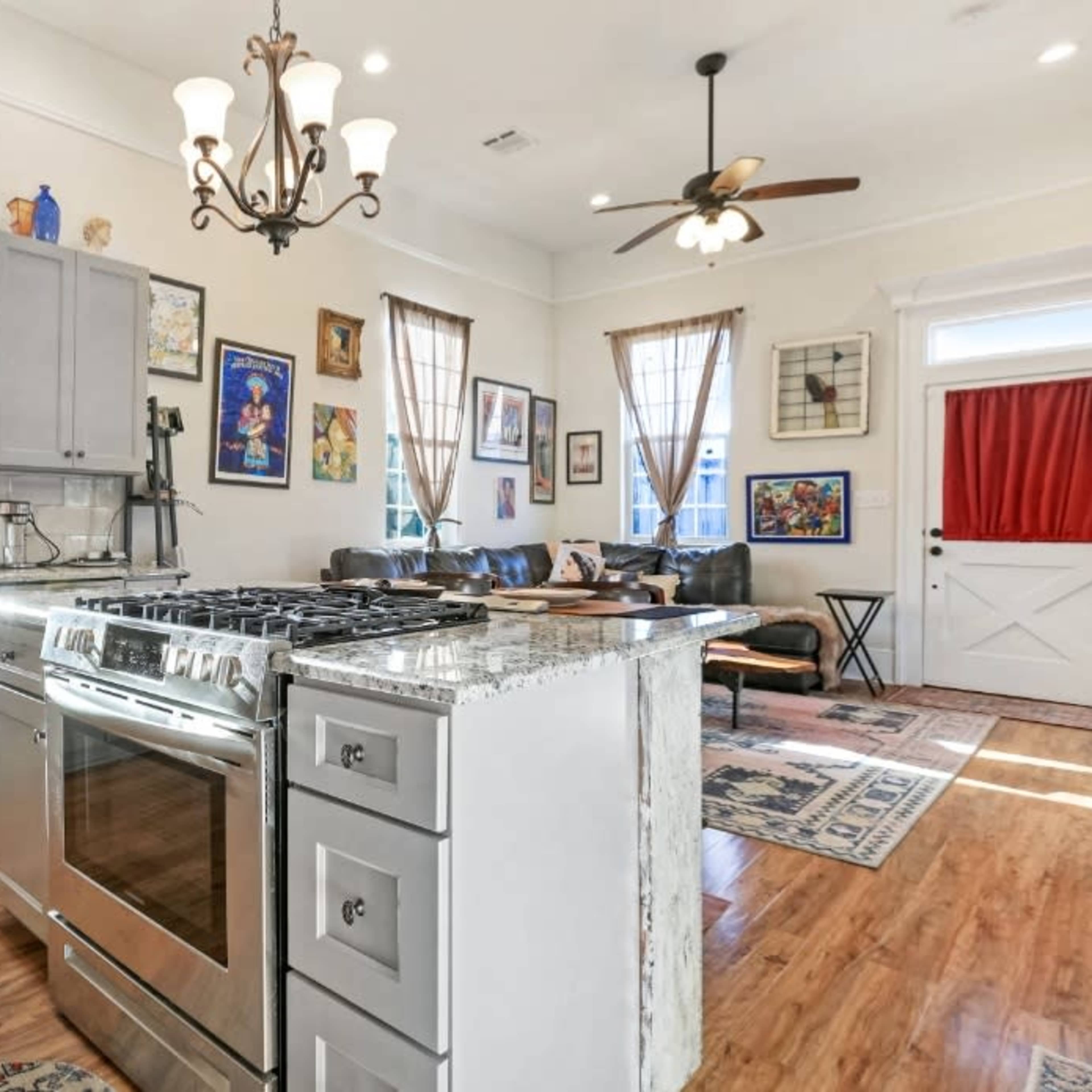 A spacious kitchen features gray cabinets, a large stainless steel stove, and a stone countertop, with a living area visible in the background.