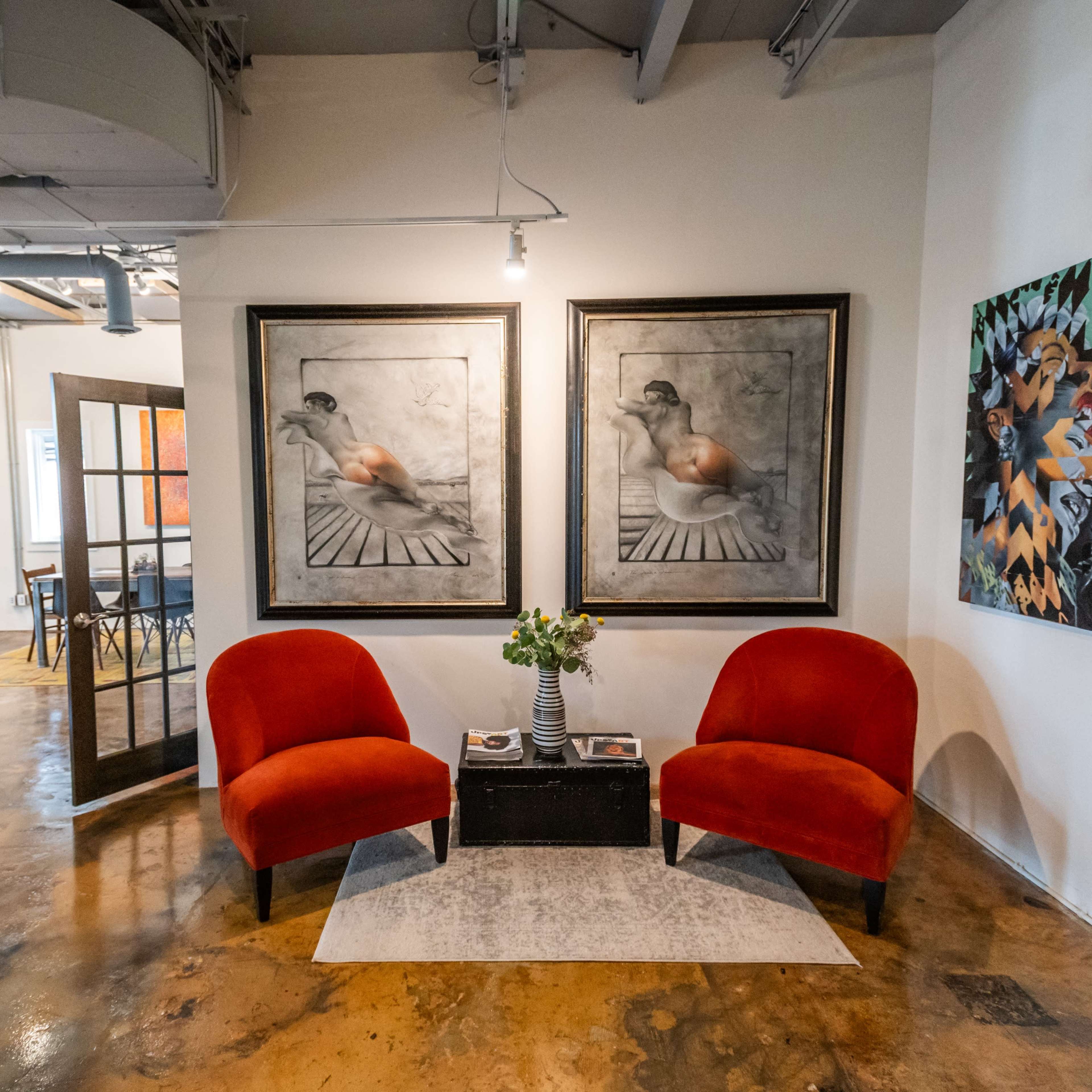 A modern interior space featuring two red armchairs, a small table with flowers, and artwork on the walls.