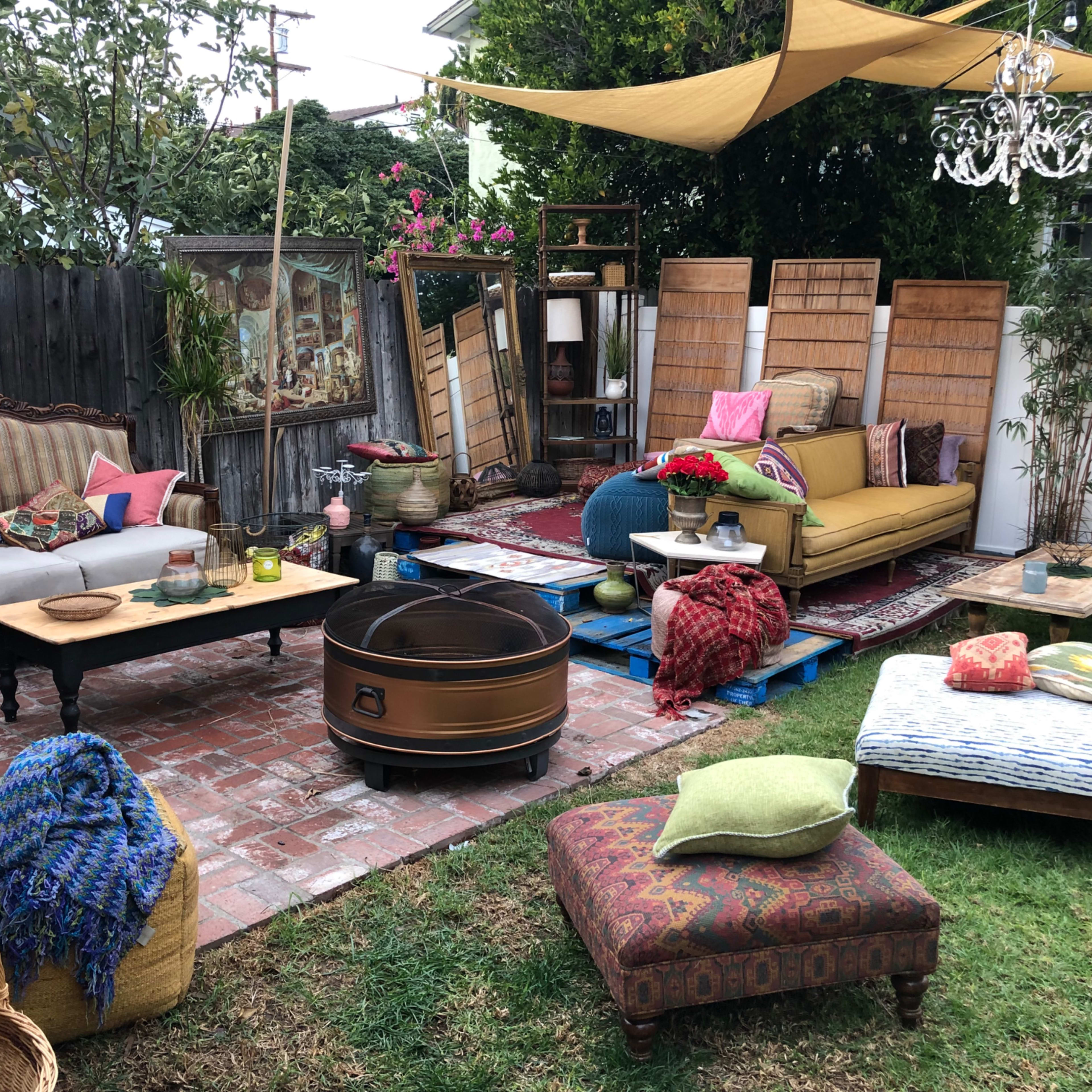 A cozy outdoor living space featuring a mix of seating options, colorful cushions, a fire pit, and decorative elements under a shaded canopy.