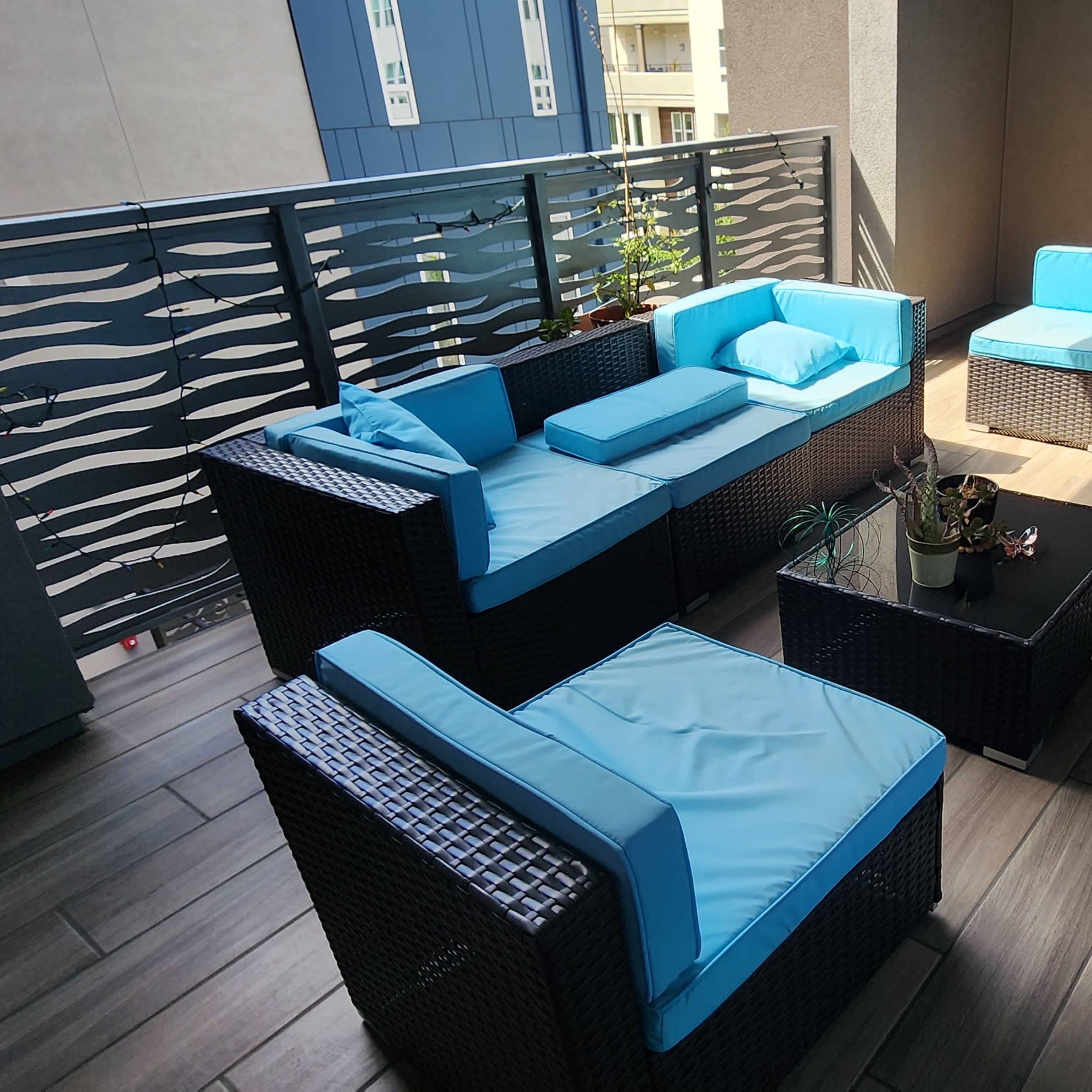 A modern balcony features wicker furniture with light blue cushions and a small potted plant on a table.