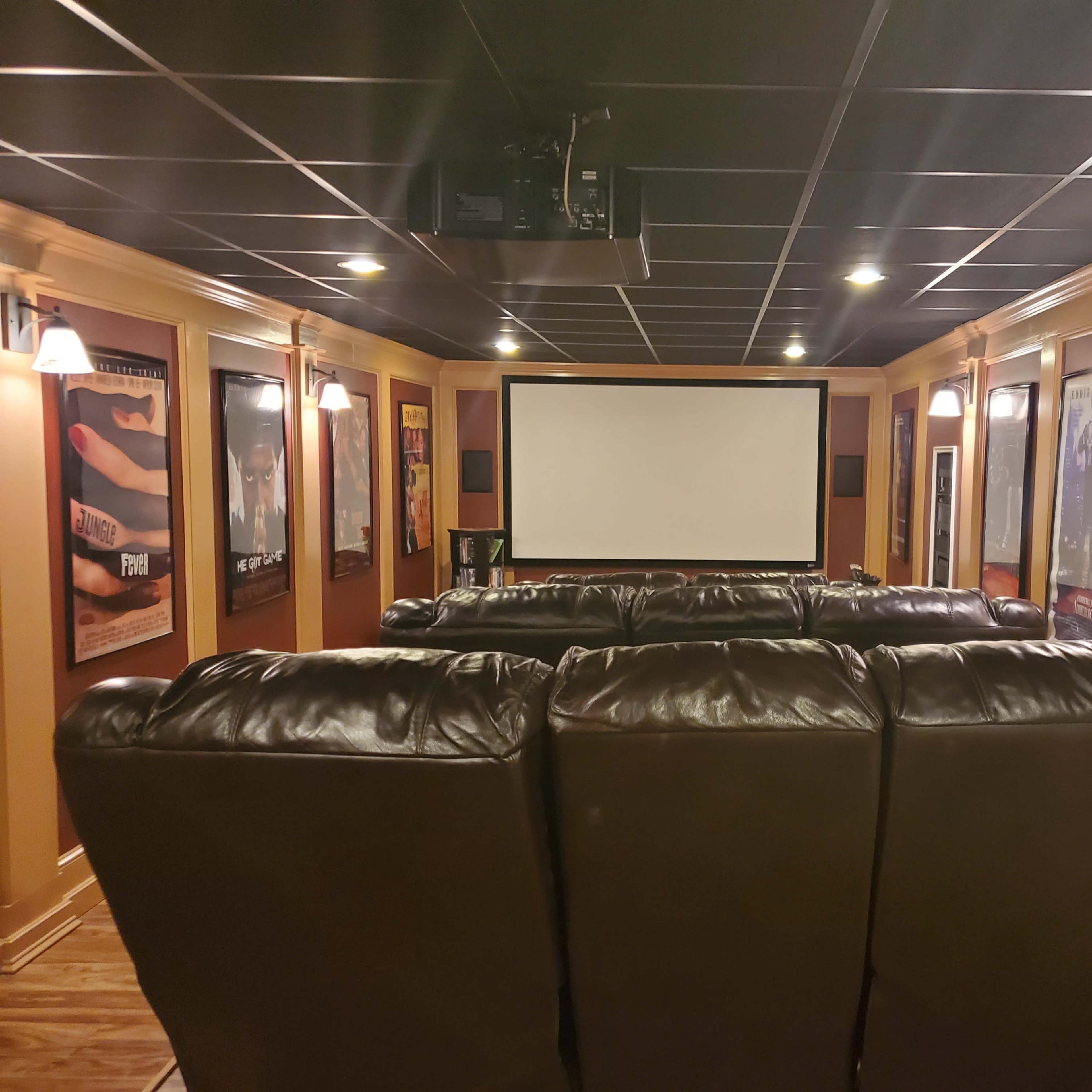 A home theater room with a large screen, leather seating, and framed movie posters on the walls.