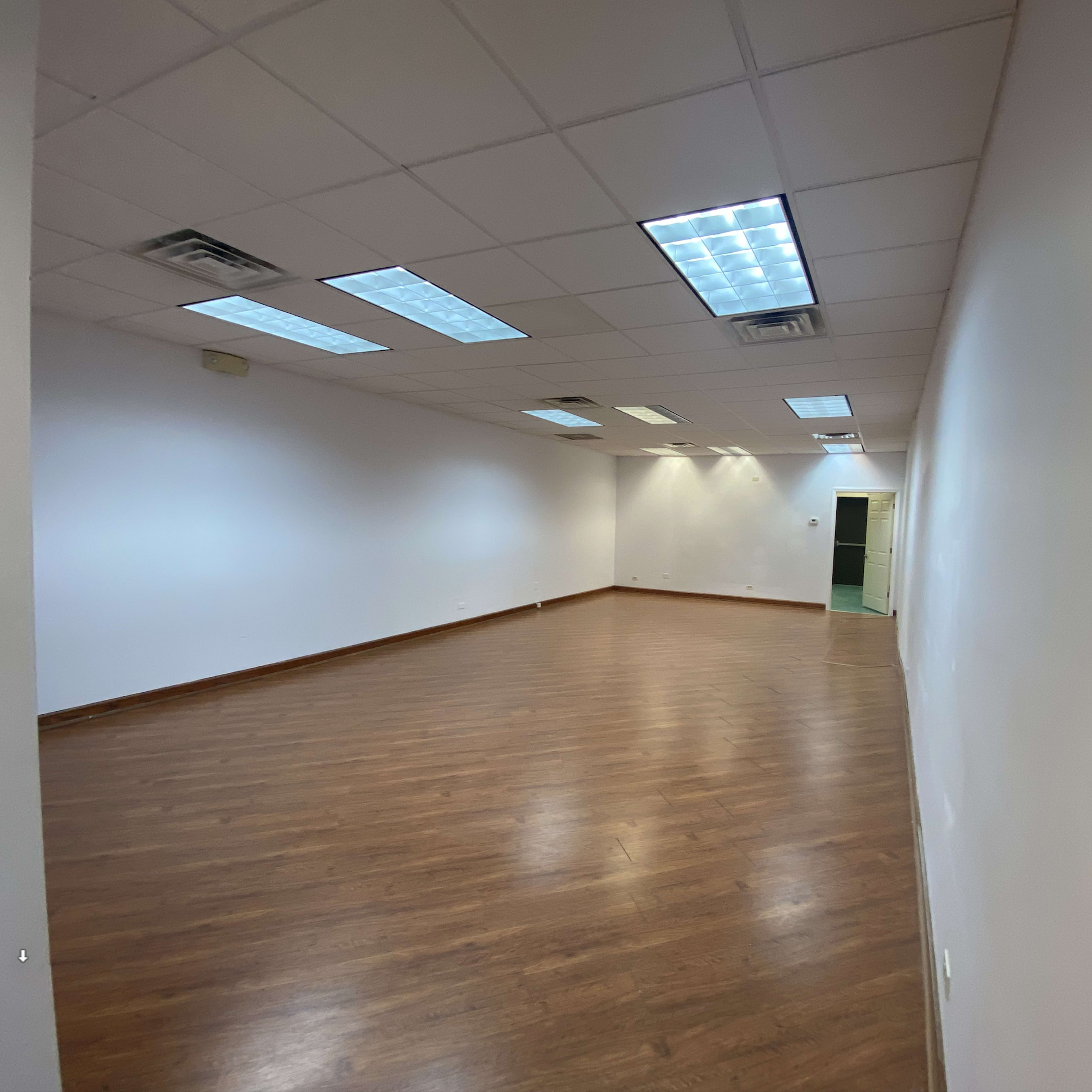 An empty room with wooden flooring, white walls, and fluorescent lighting.