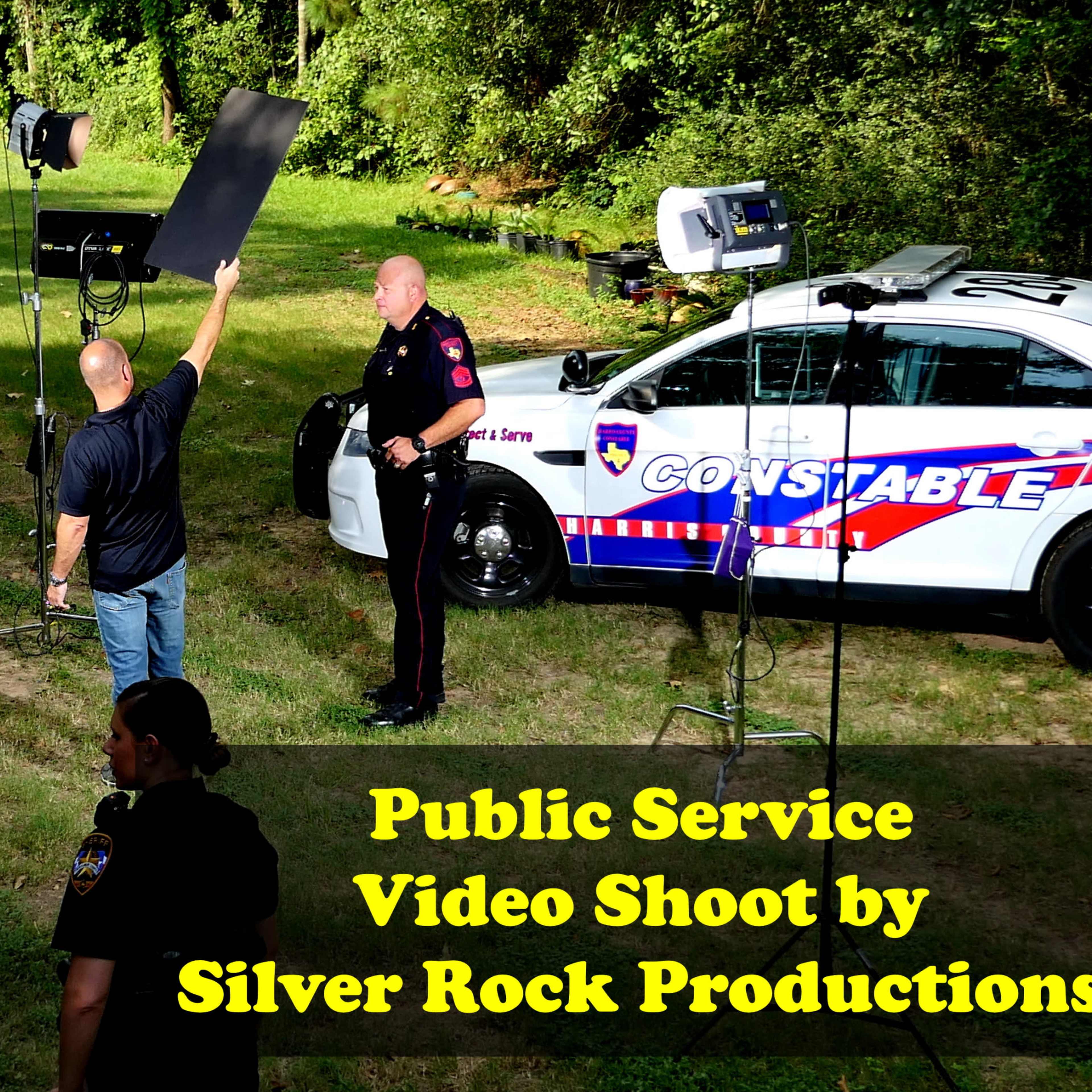 A group of people is filming a public service video in a grassy area, featuring law enforcement personnel and production equipment.
