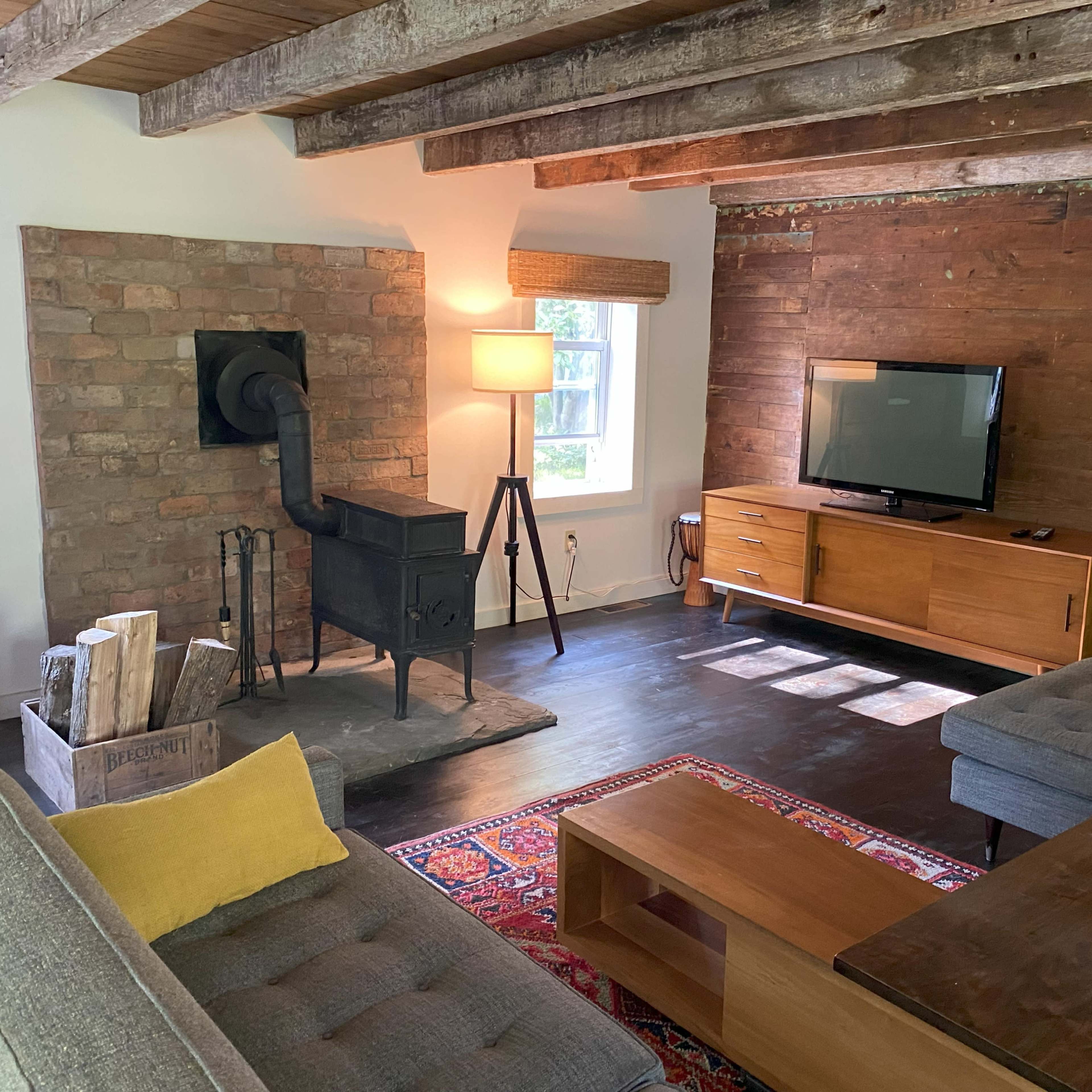 A cozy living room featuring a wood stove, a television on a wooden cabinet, and two gray sofas arranged around a coffee table.