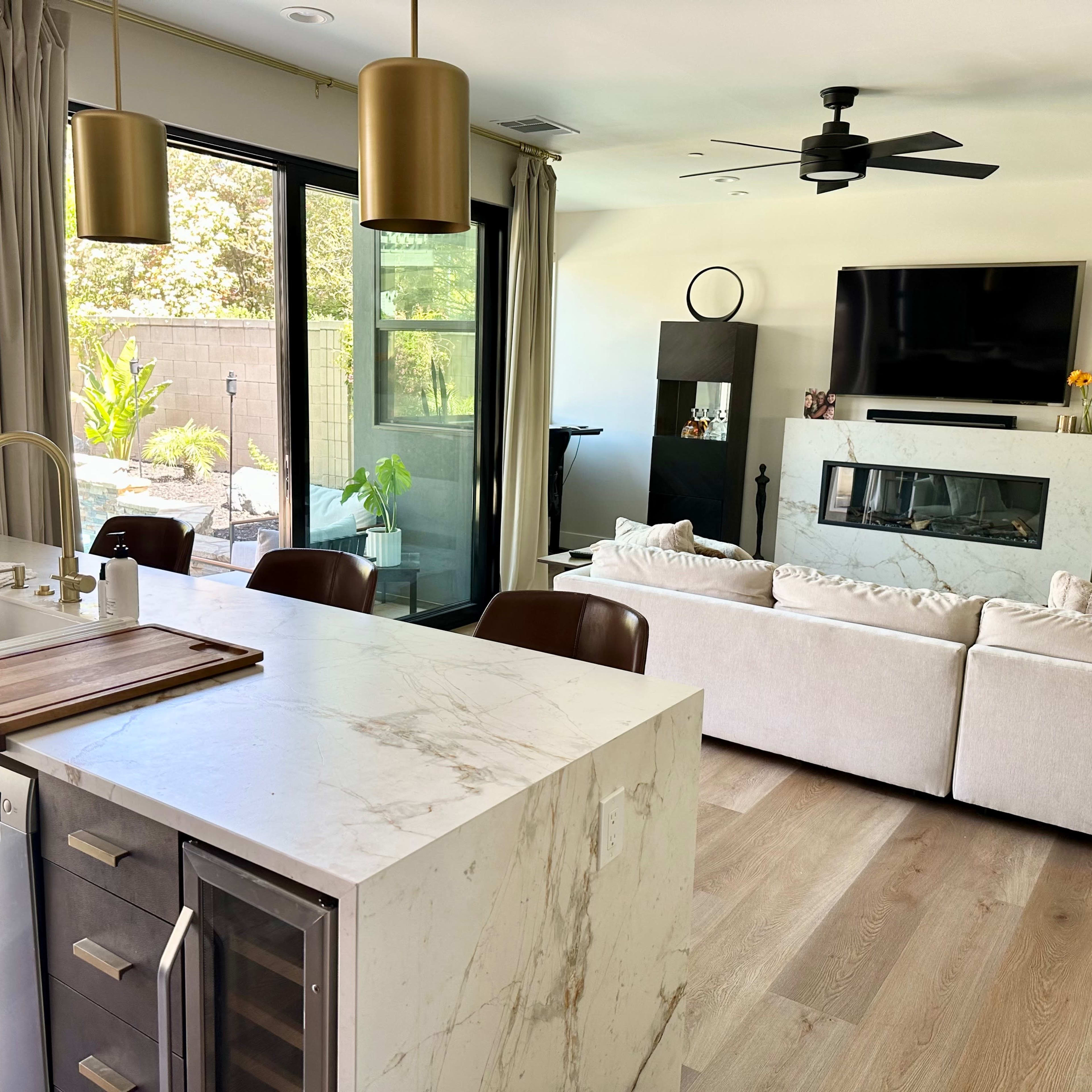 A modern living space featuring a kitchen with a marble countertop and an open layout connecting to a cozy living area with beige sofas.