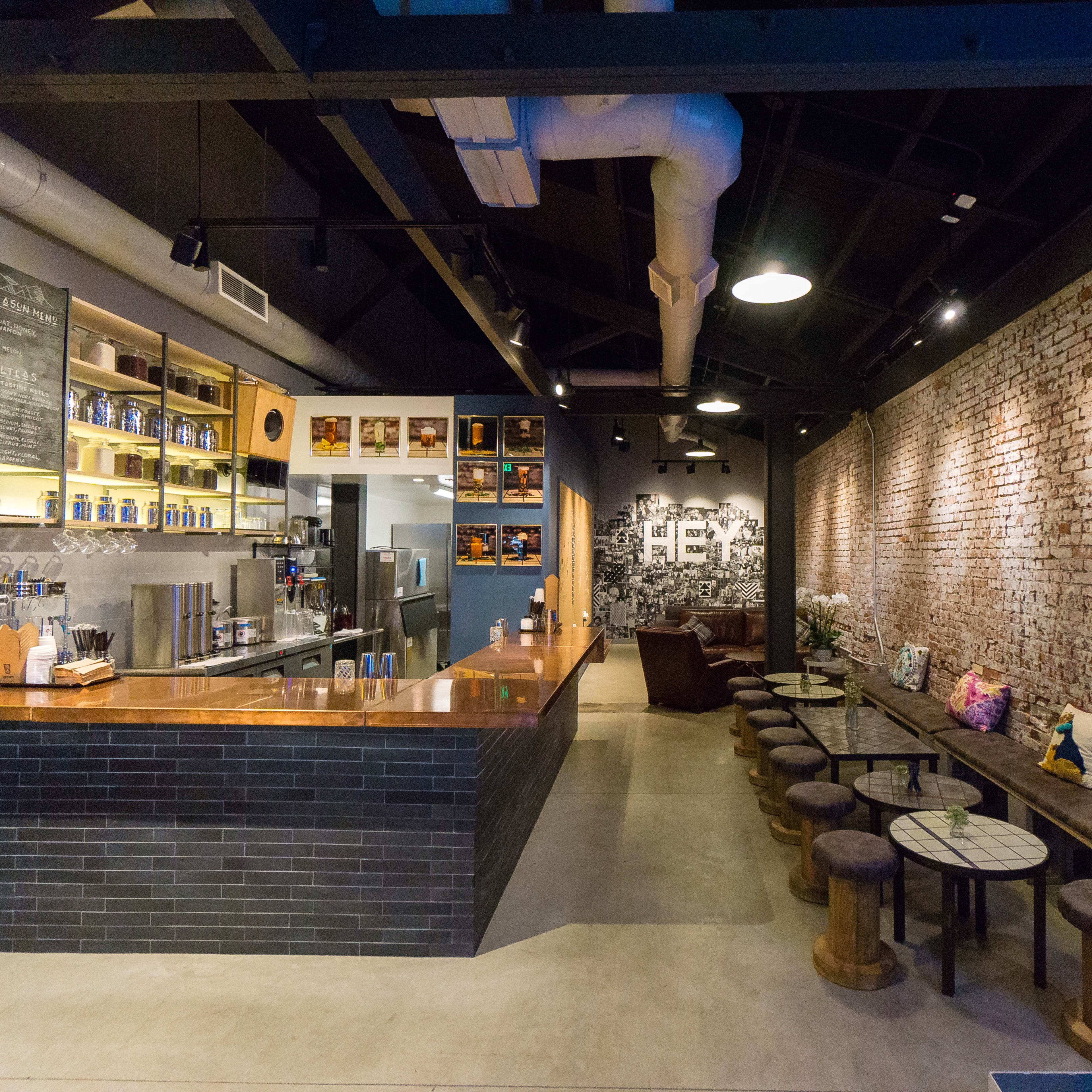 A modern café interior with a brick wall, wooden seating, a counter displaying coffee equipment, and decorative elements on the shelves.