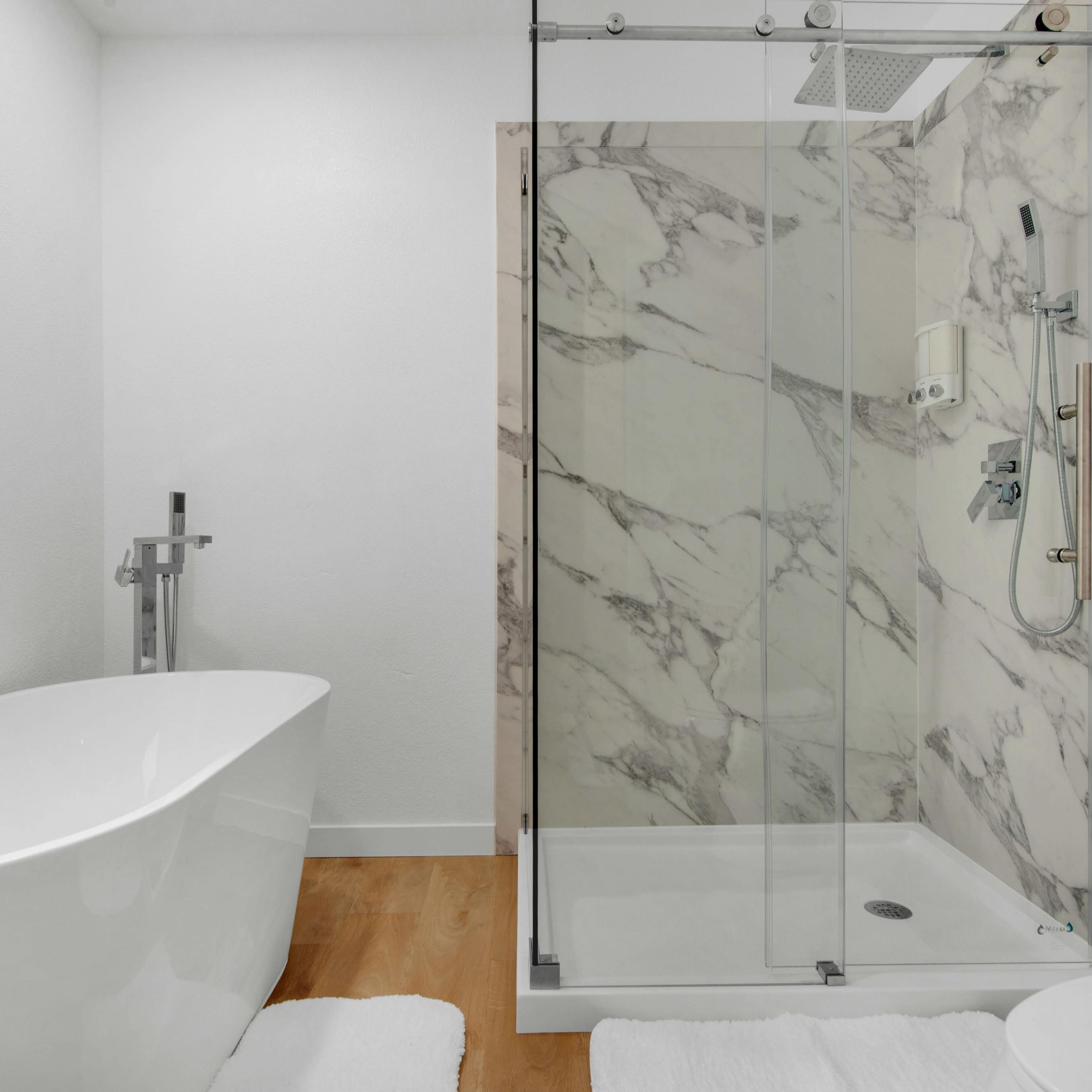 A modern bathroom featuring a freestanding bathtub, a glass-enclosed shower with marble walls, and wooden flooring.