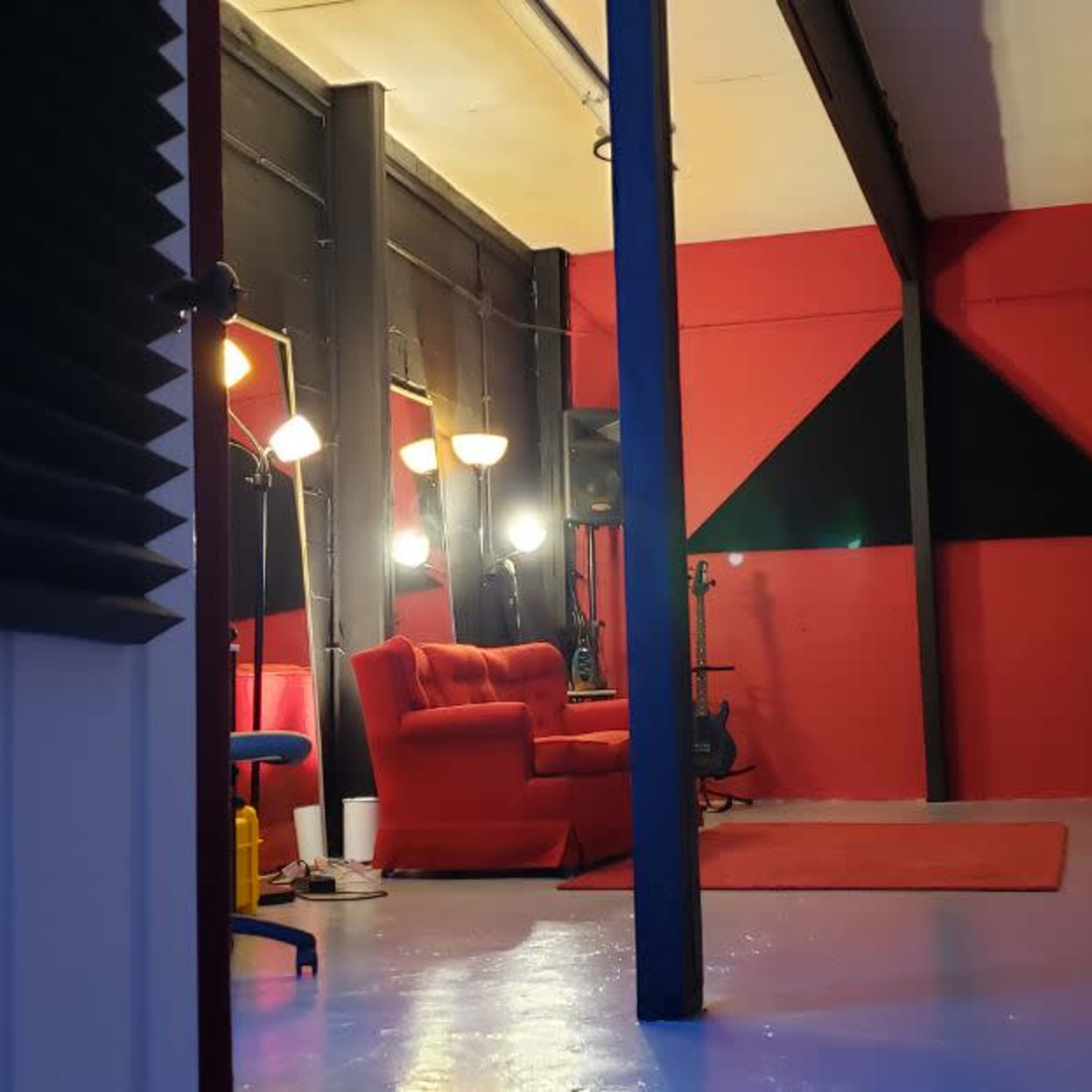 A room with red walls, a red couch, and various lighting fixtures, with chairs and a stool positioned around the space.