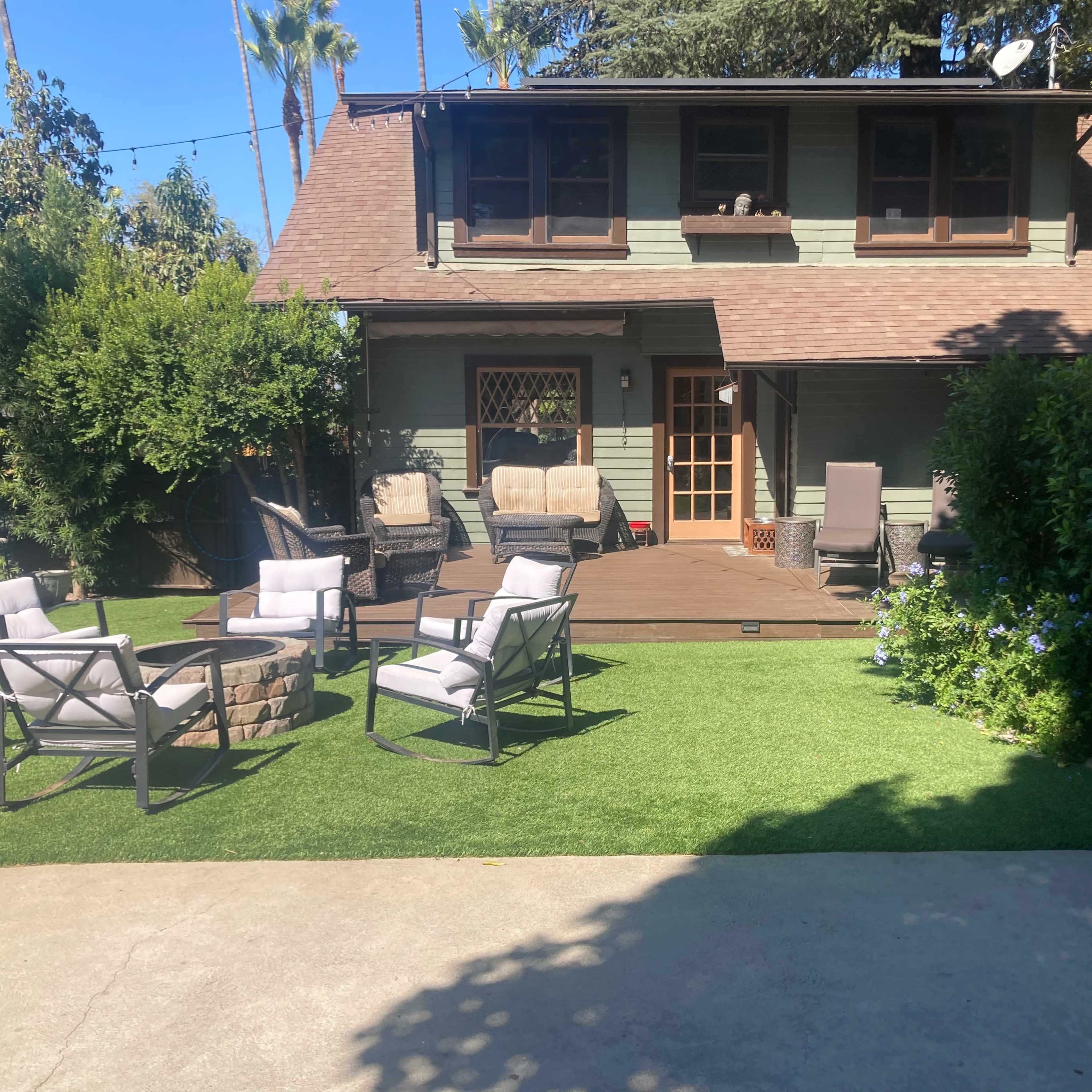 A backyard scene with a deck and outdoor seating arrangement in front of a two-story house.