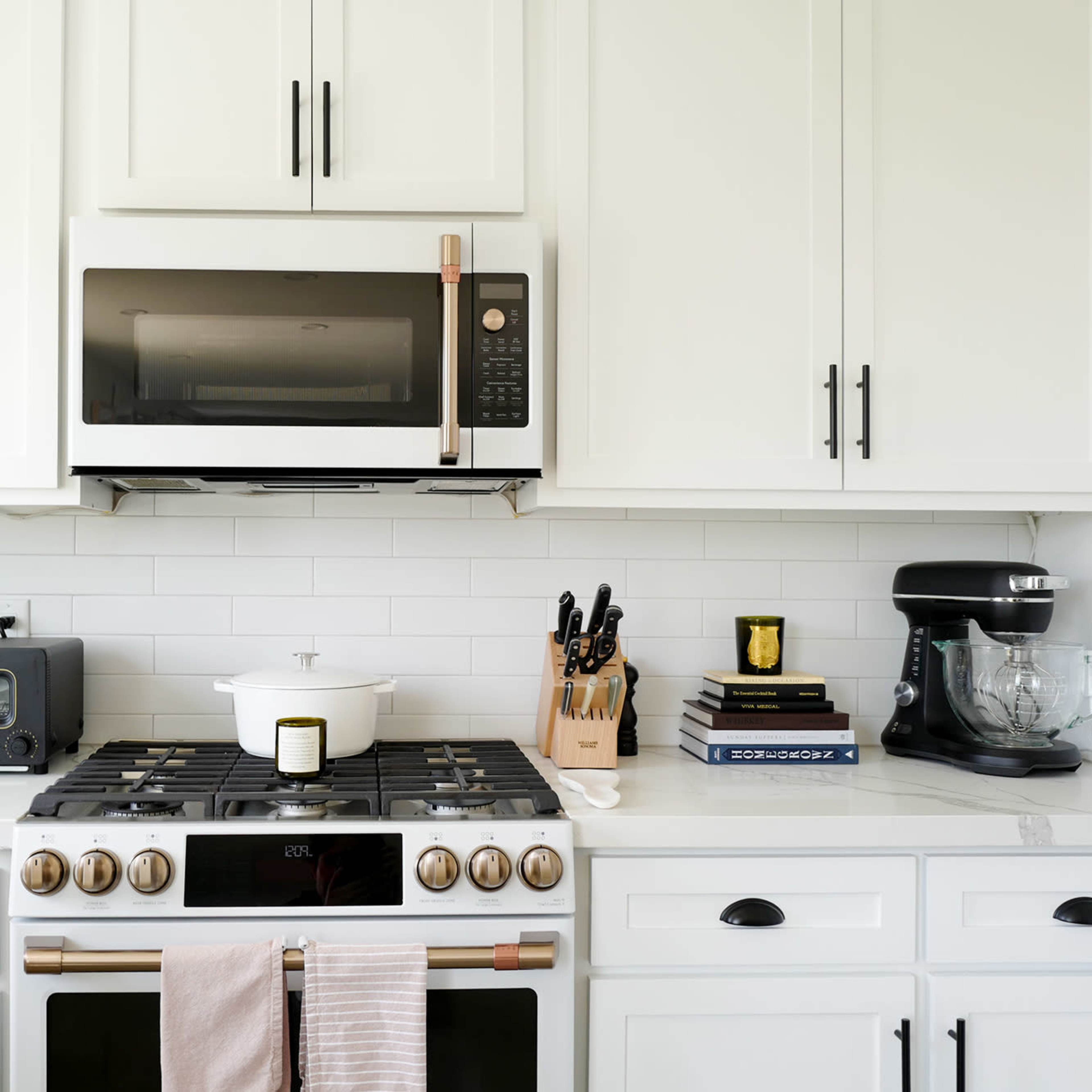 A modern kitchen with white cabinetry, a stainless steel microwave above a gas stove, and various kitchen appliances and tools arranged on the countertop.