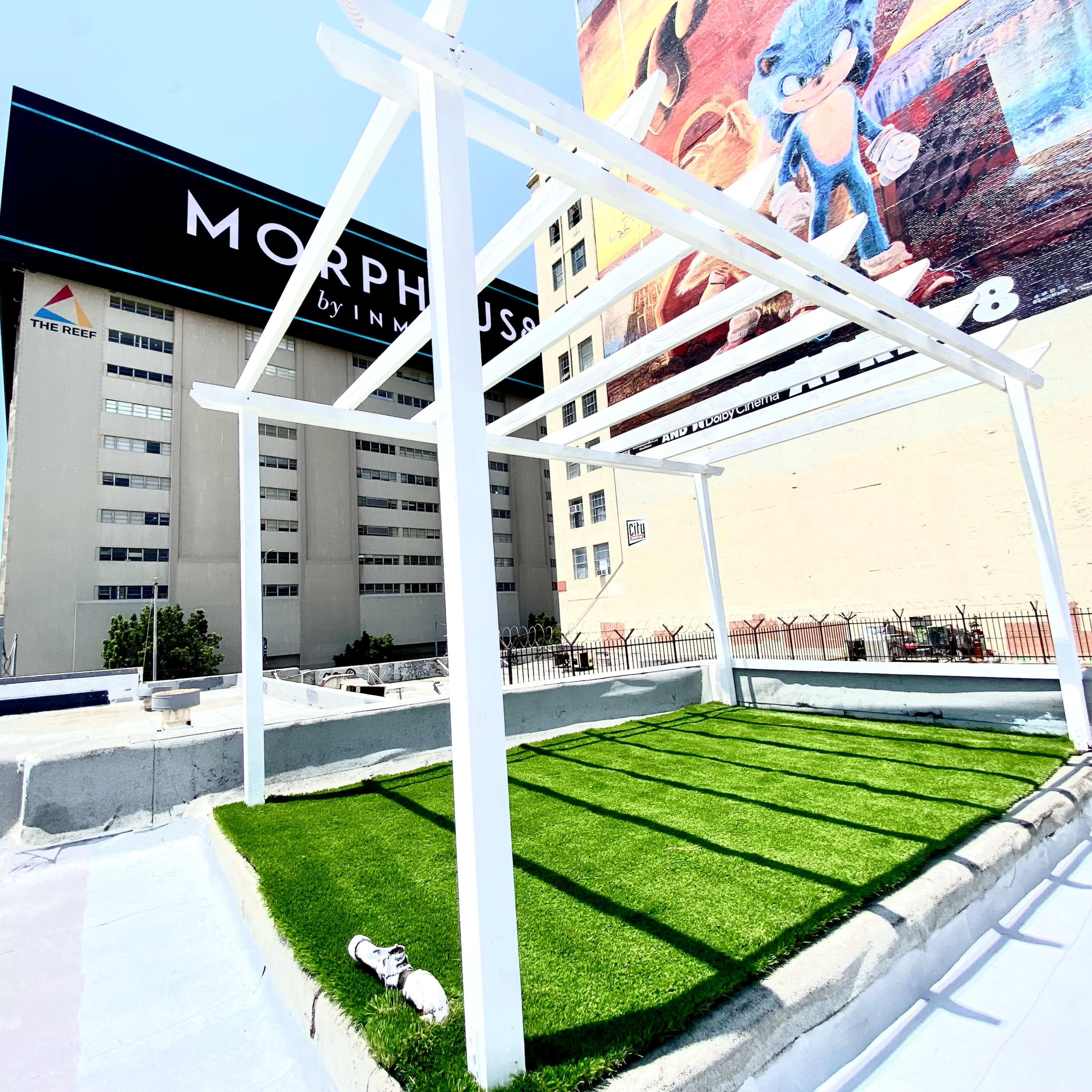A rooftop space with a green artificial lawn and a white framework, set against a large mural featuring a cartoon character.