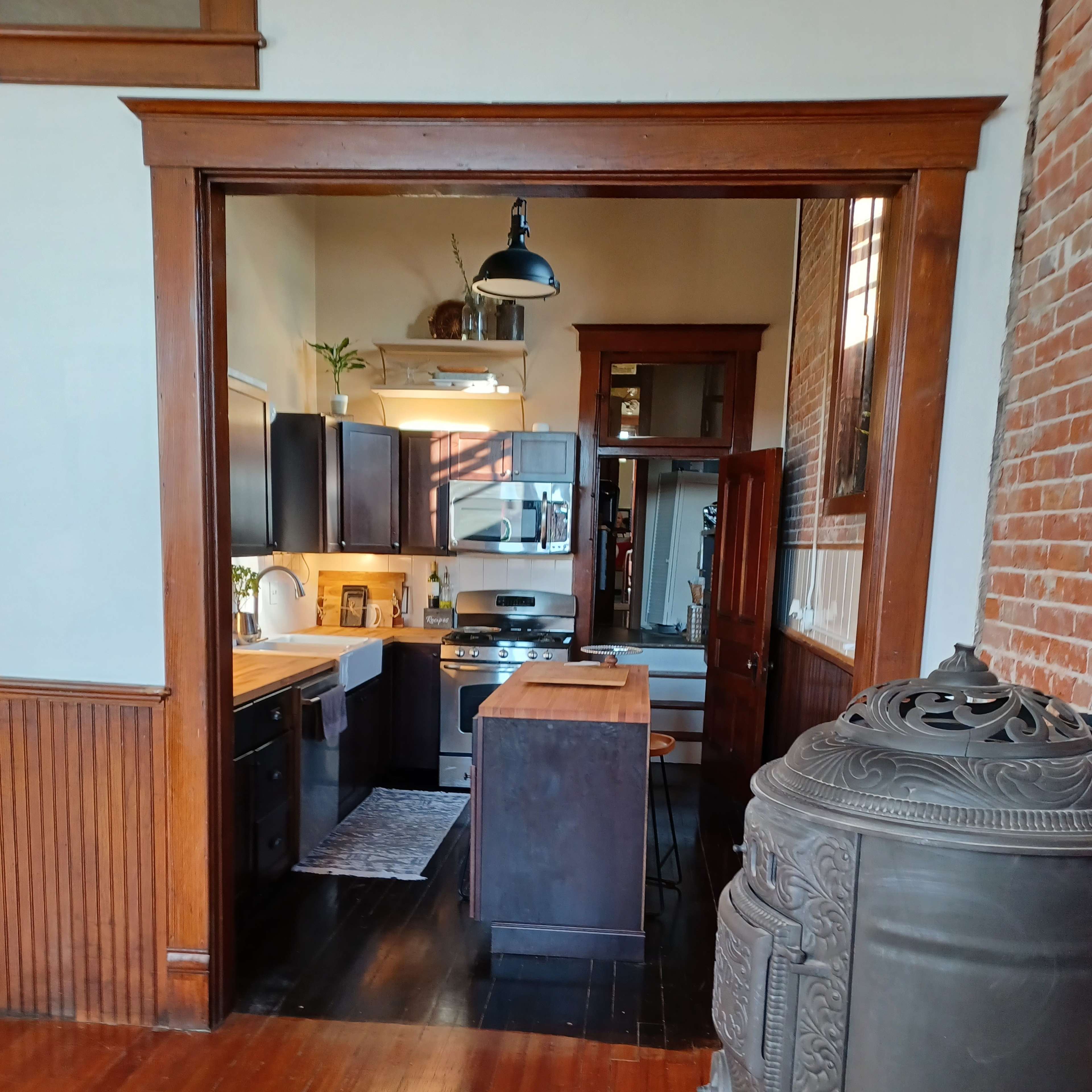 A kitchen area featuring modern appliances, an island, and a vintage stove, framed by a wooden entryway with exposed brick walls.