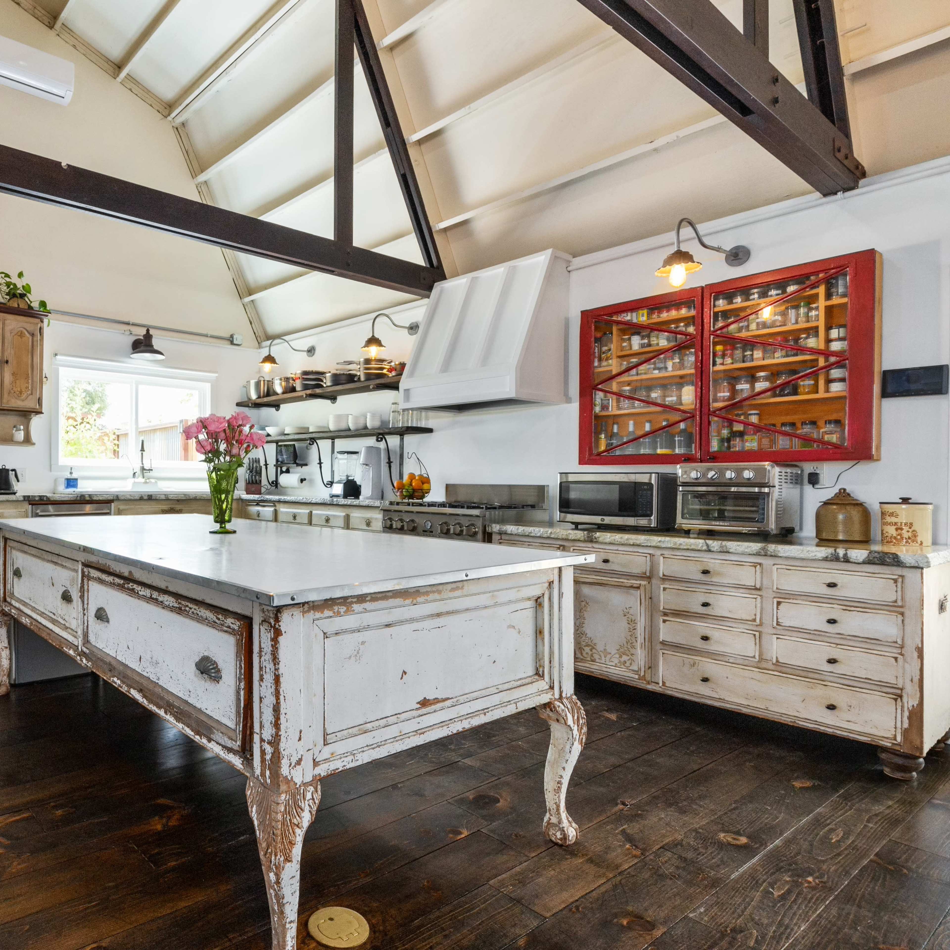 A spacious kitchen with a large central island, wooden floors, and high, slanted ceilings, featuring a mix of modern and vintage appliances.