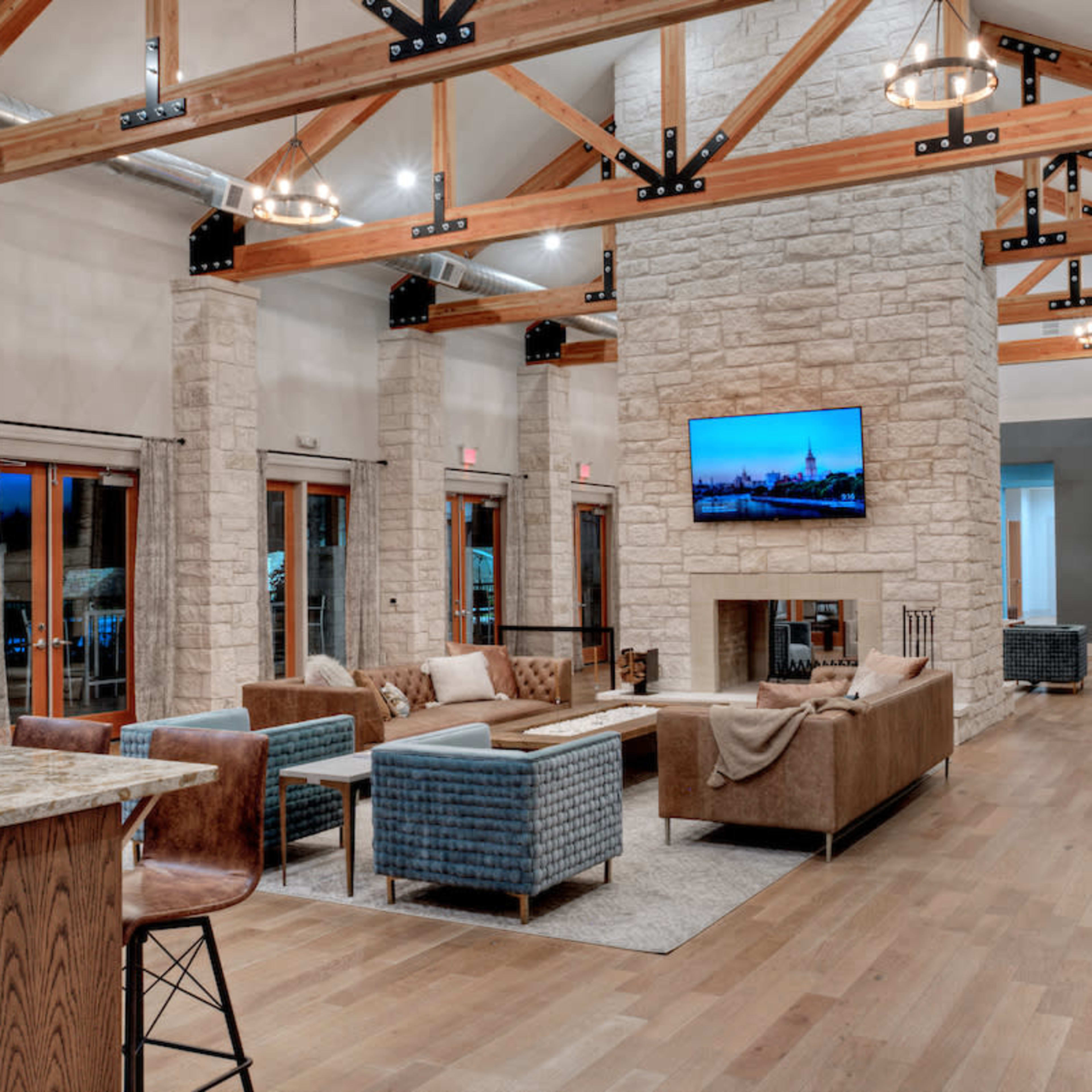 A spacious interior lounge area with stone walls, wooden beams, and a large television mounted above a fireplace, accompanied by comfortable seating arrangements and a pool table.