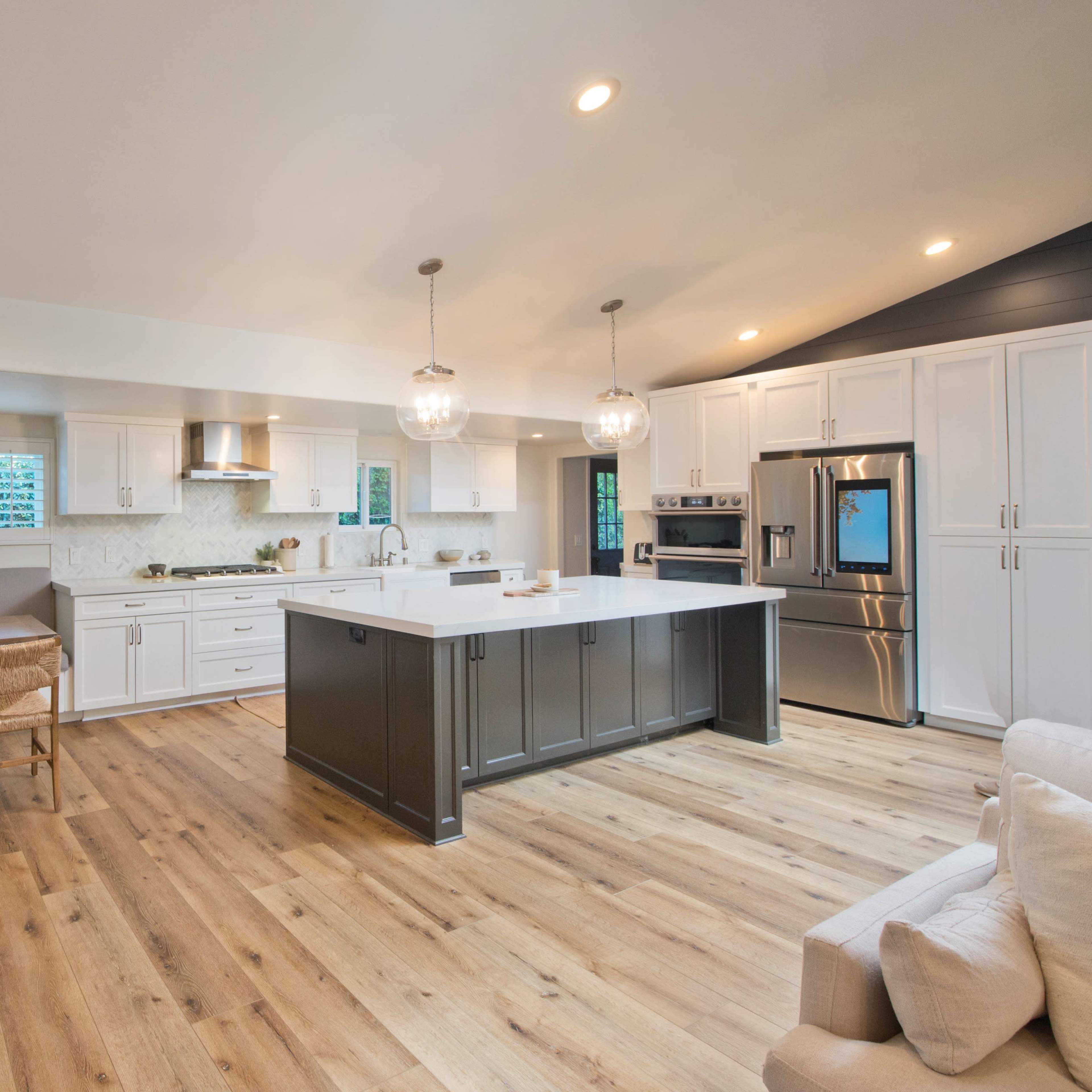 A modern kitchen layout with white cabinets, a central island, and a dining area featuring a built-in bench and wooden chairs.
