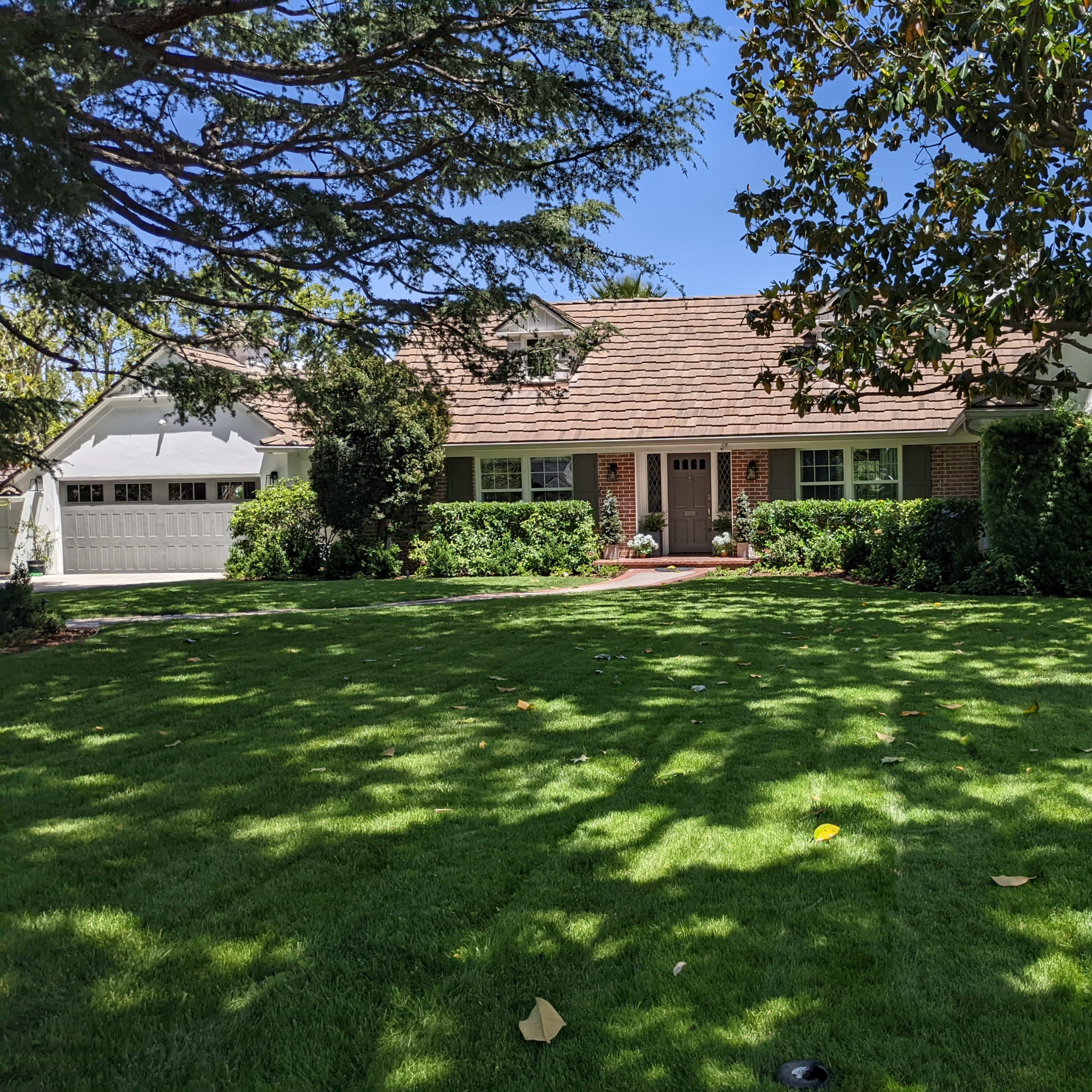 A front view of a house with a manicured lawn and trees surrounding it.