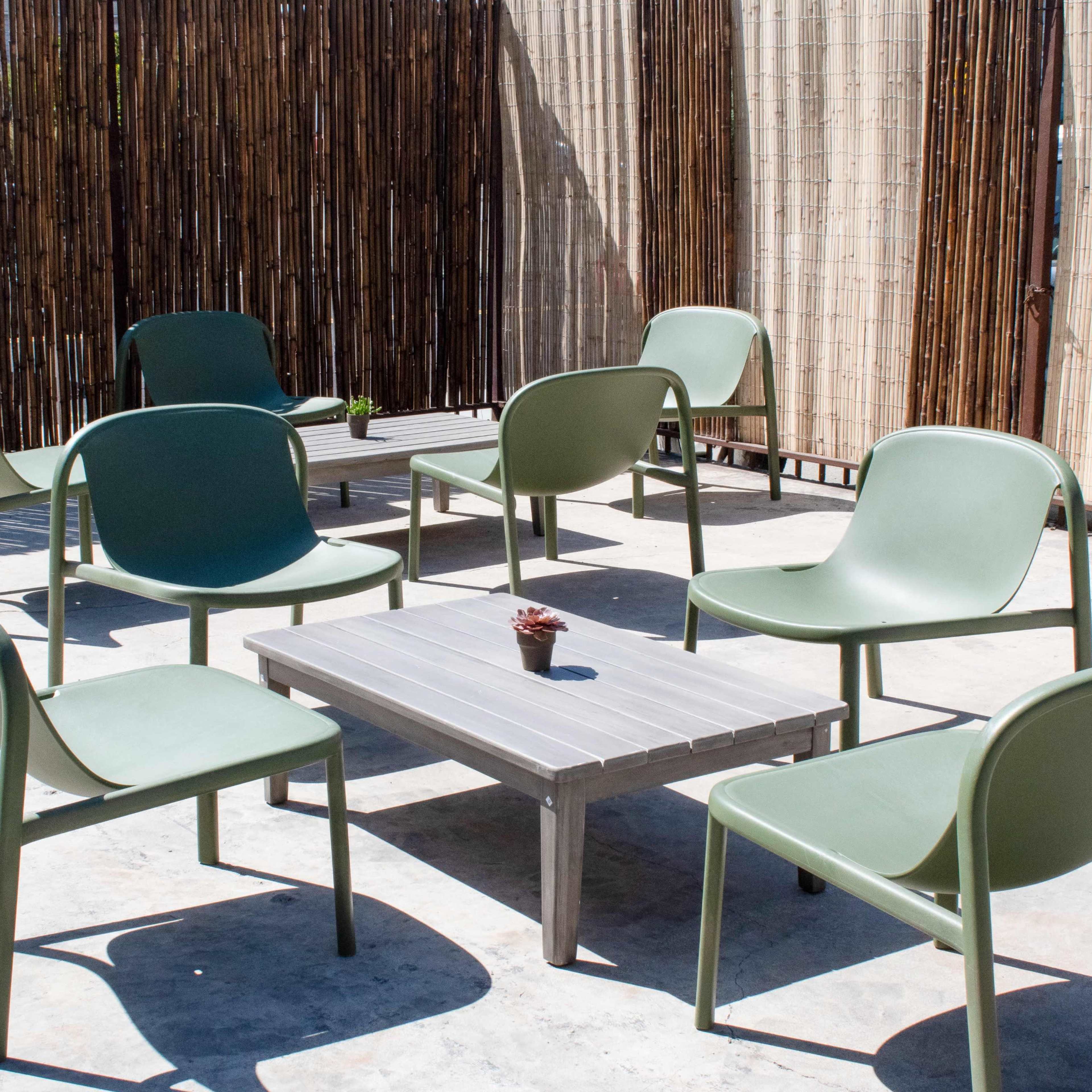 A circular arrangement of green chairs surrounds a metal table on a concrete surface, with a bamboo privacy screen in the background.